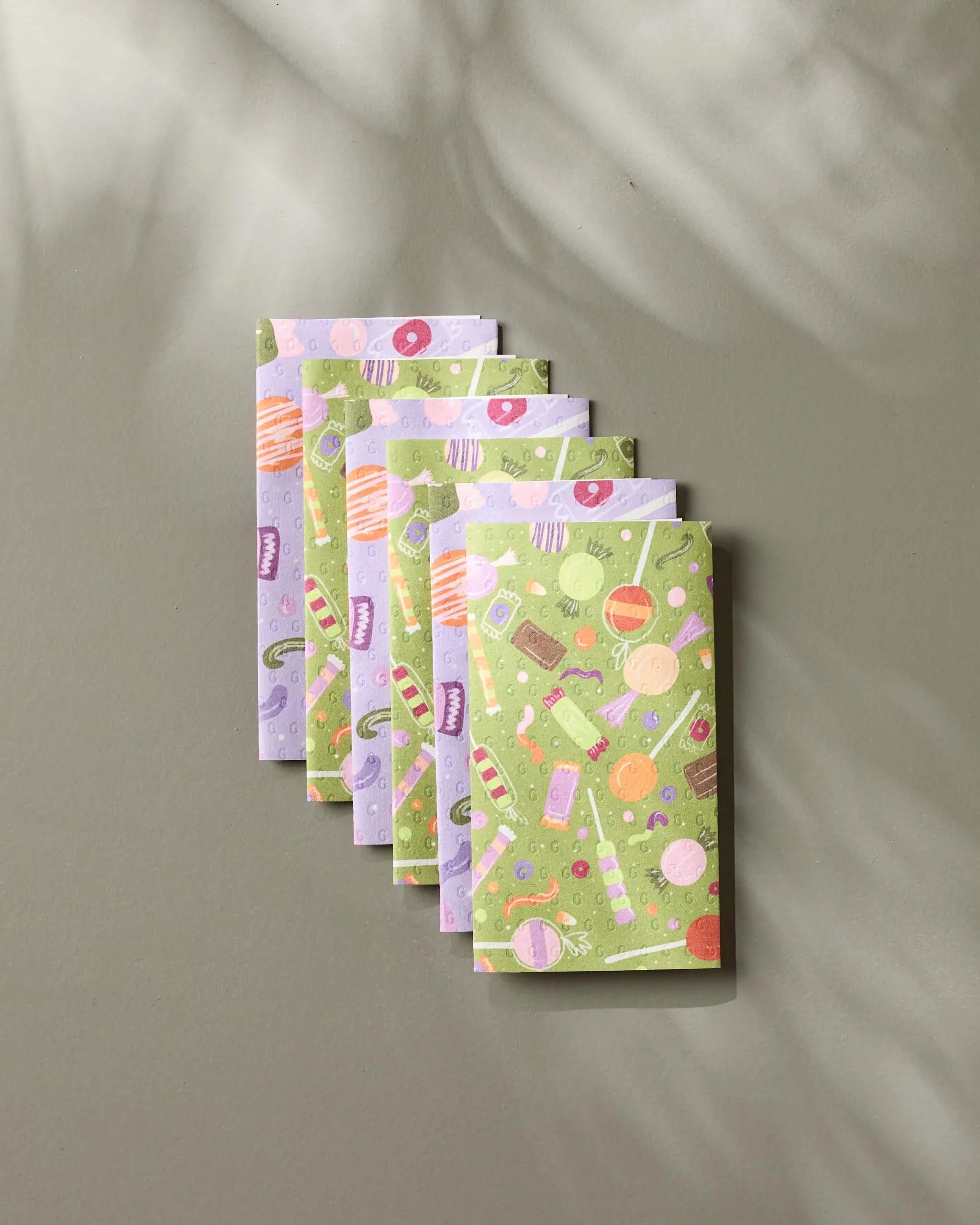 Six Sweet Treasures reusable paper towels by Geometry, featuring pastel green and lavender candy patterns, are neatly stacked on a light surface with soft background shadows.