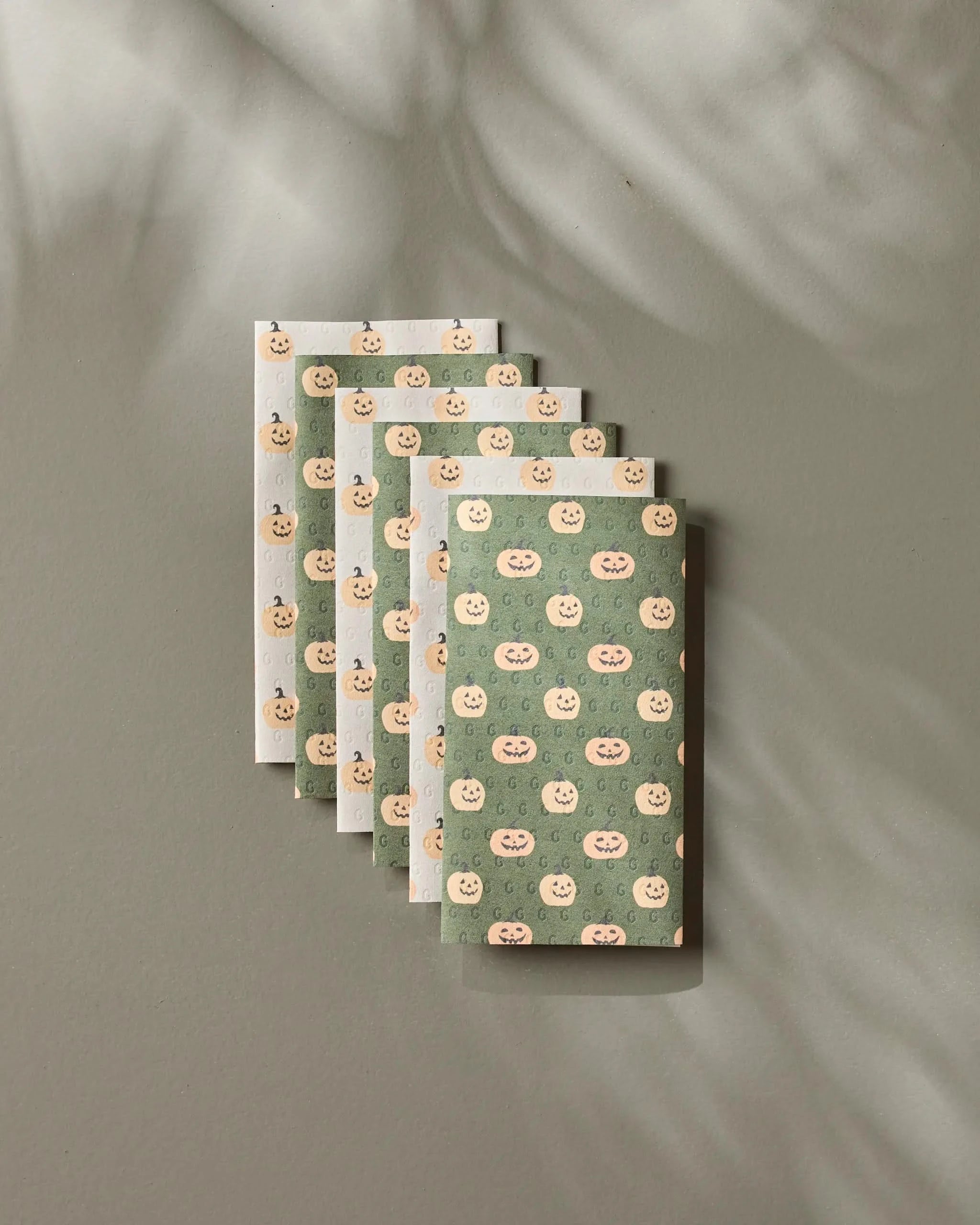 Six Spice and Smiles notebooks by Geometry, featuring a smiling peach pattern on pastel green and white covers, are arranged diagonally on a gray surface with soft shadows for an eco-friendly look.