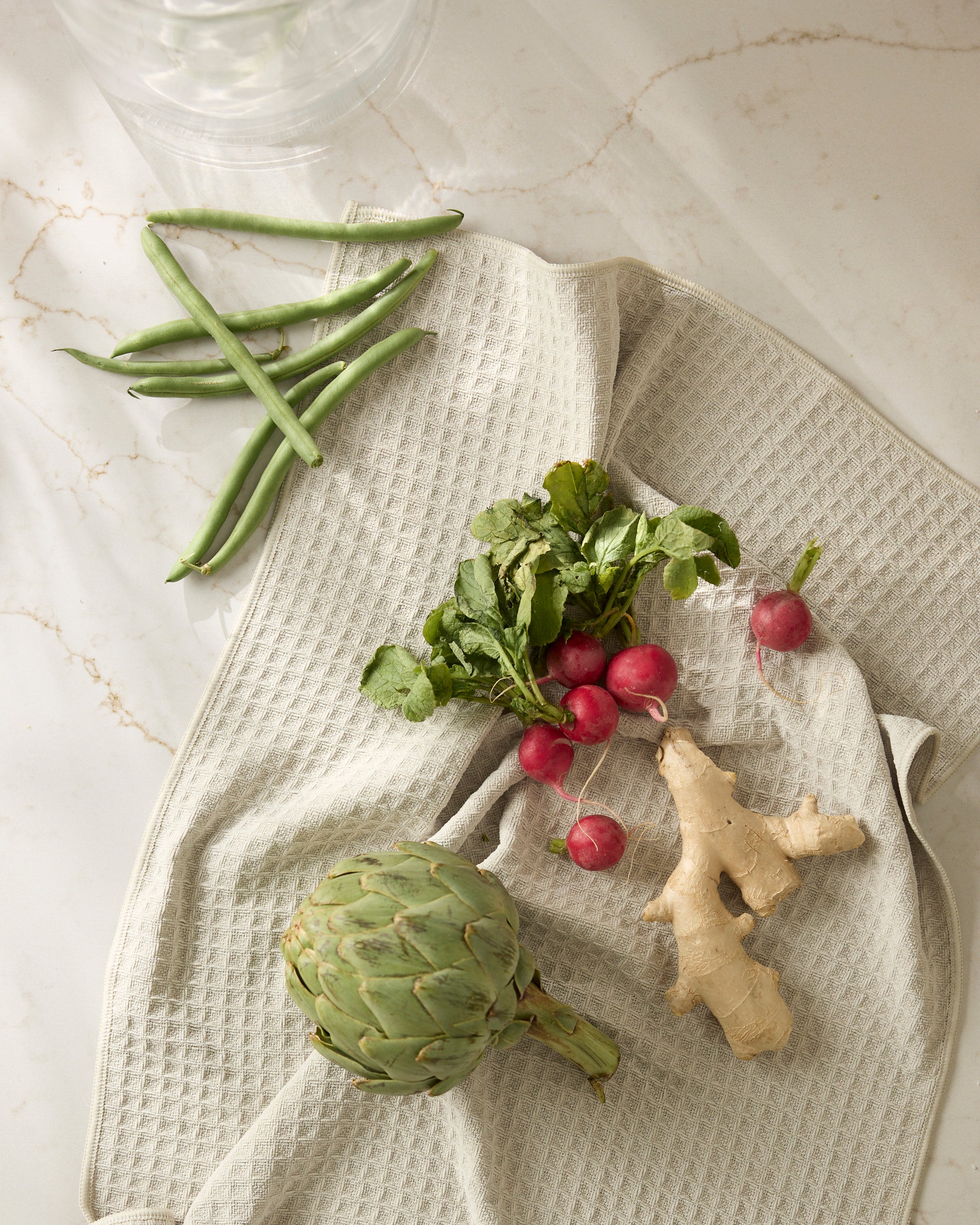 Geometry’s Vanilla towel is displayed on a beige textured cloth atop a marble surface, with soft natural light casting gentle shadows.