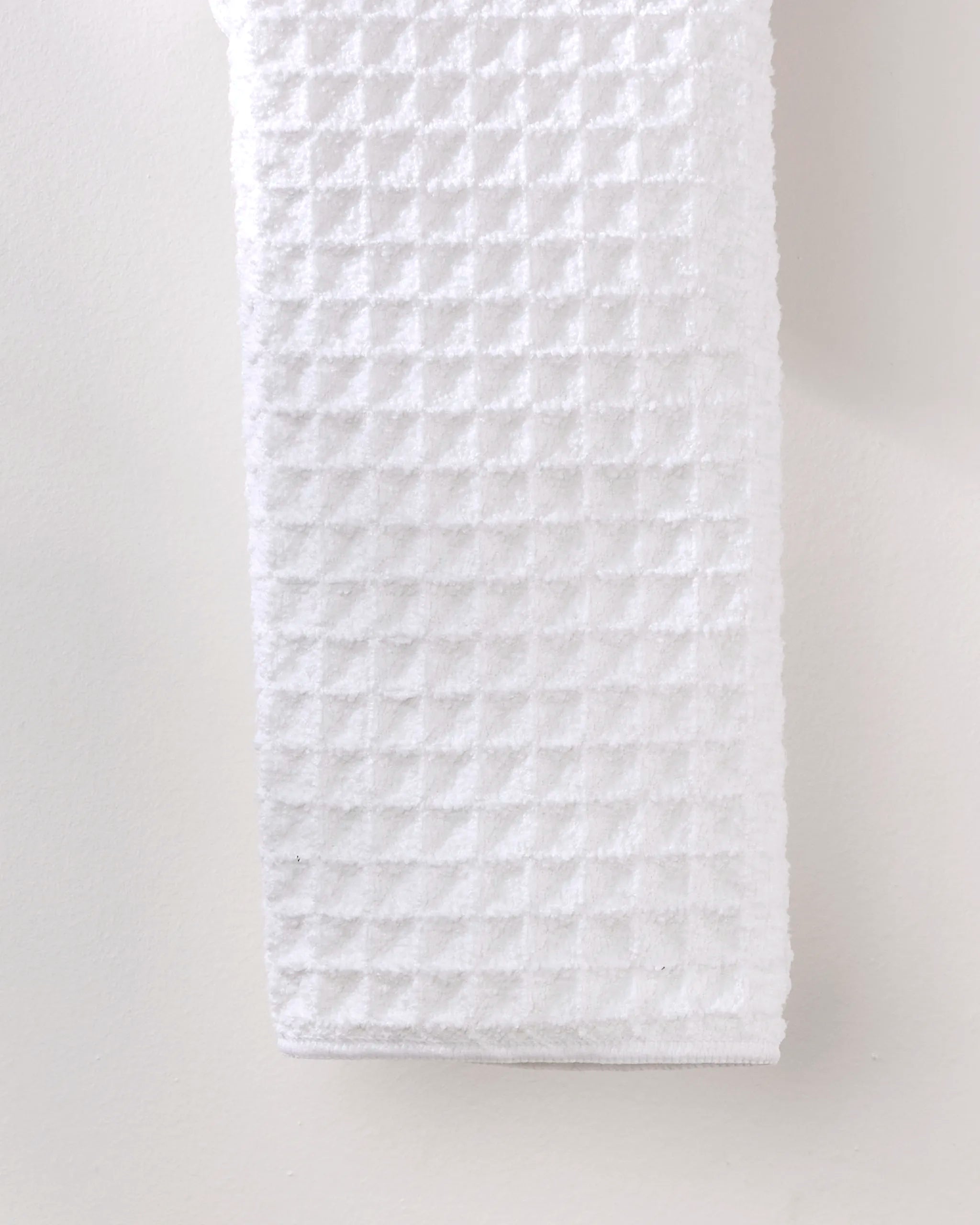 The GEOMETRY Cloud waffle hand towel, made from recycled materials, hangs vertically against a plain, light-colored wall.