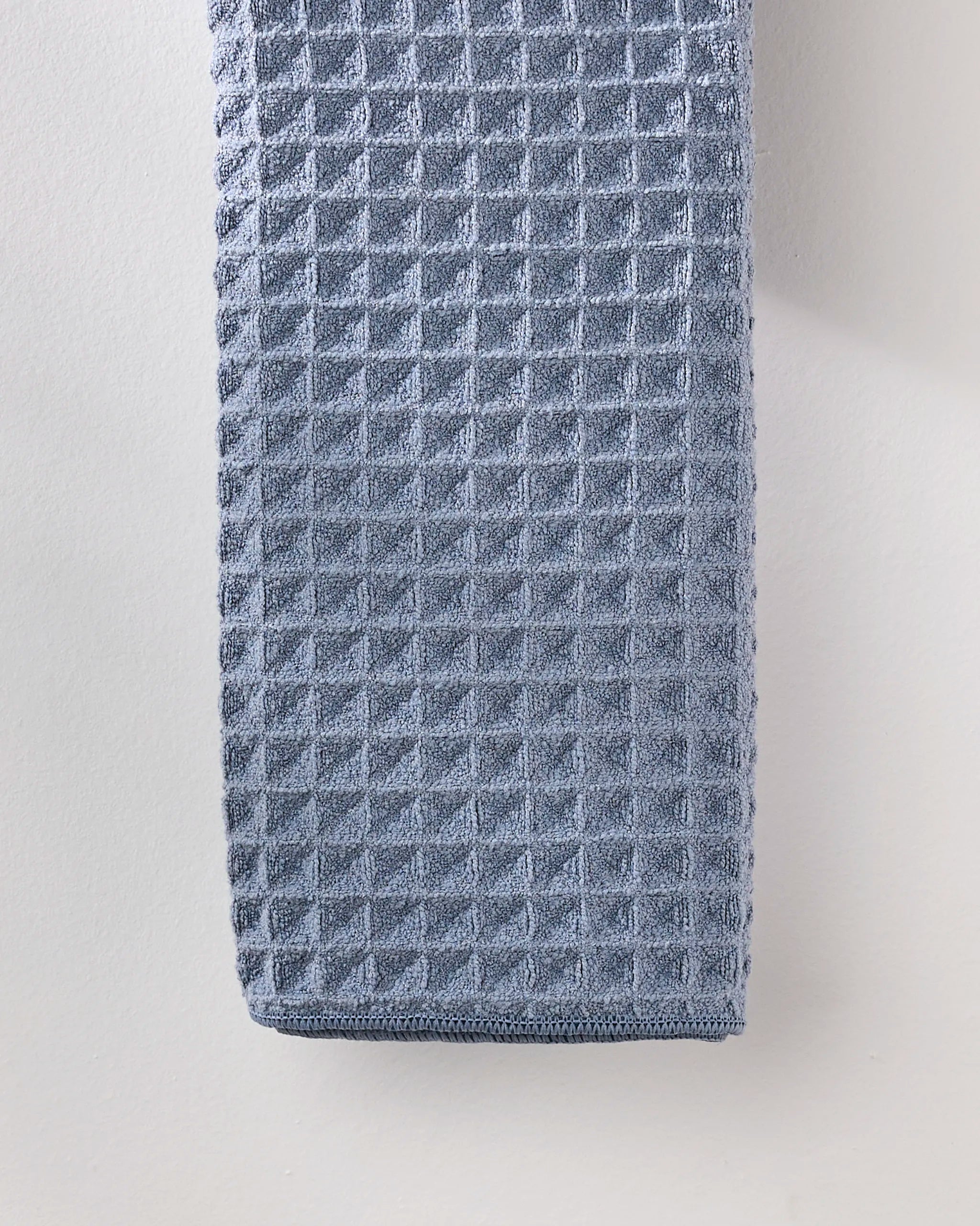 A close-up of the neatly folded GEOMETRY Sky waffle hand towel, featuring a textured finish, hanging against a light-colored wall.