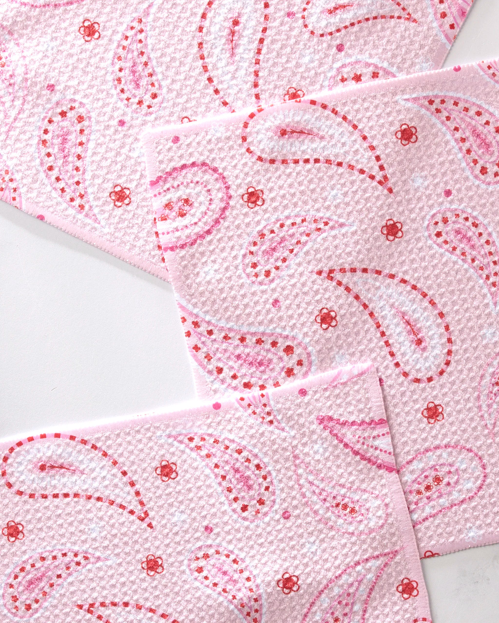 Three overlapping sheets of GEOMETRY Sweet Paisley pink textured paper towels made from recycled materials, featuring red and pink paisleys with small red flowers on a white background.