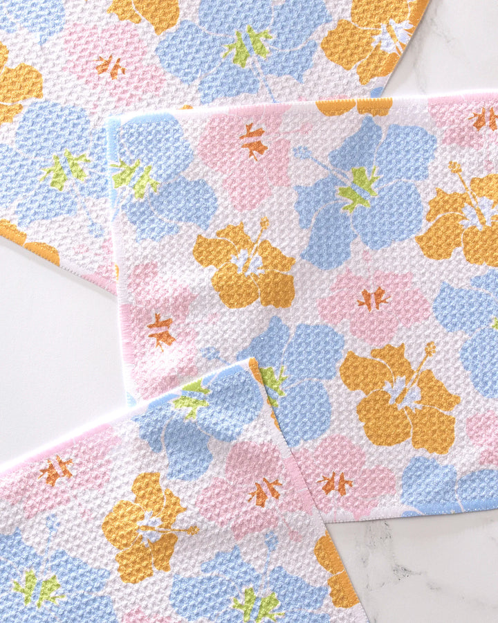 GEOMETRY’s Hula Hues set includes three super-absorbent dish towels made from recycled materials, each featuring pastel blue, pink, yellow, and green floral patterns reminiscent of hibiscus flowers.