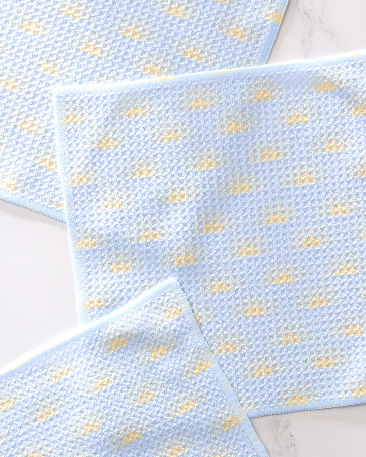 Three light blue GEOMETRY "Soft Summer Sun" dishcloths with a yellow cloud pattern and matching blue borders are neatly arranged on a white surface, showcasing their soft, super-absorbent woven design.