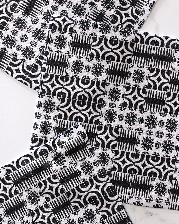 Four Bohemian Mosaic coasters by GEOMETRY, featuring black and white geometric and floral designs on recycled materials, are arranged with overlapping corners on a light surface.