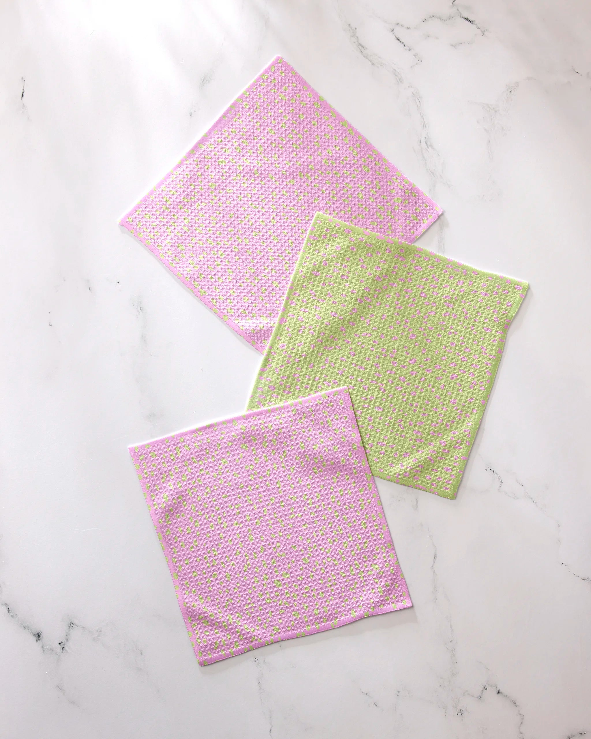 Three square washcloths from GEOMETRY’s Speckle Green Pink set—two pink with multicolored dots, one light green with pink, yellow, and white dots—made from recycled materials and crafted for super absorbency.