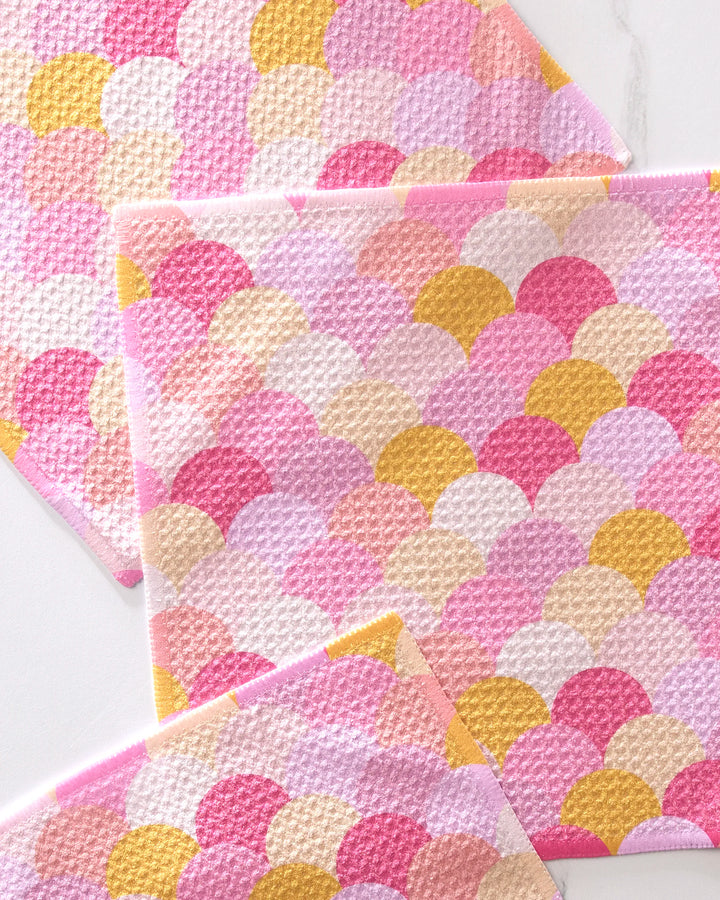 The GEOMETRY Inherit set features three eco-friendly dishcloths with a pink, yellow, and white scallop pattern, crafted from recycled materials and stylishly layered against a white background.