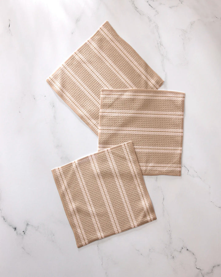Three GEOMETRY Vanilla Chai beige and white striped textured recycled dishcloths overlap on a white marble surface.