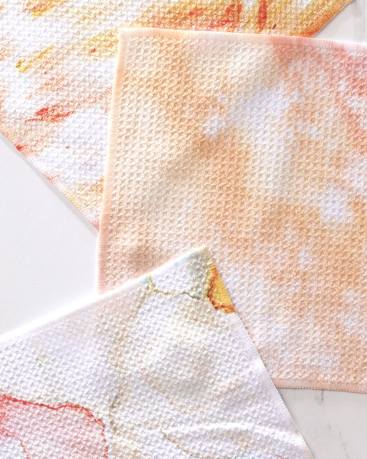 The GEOMETRY Nice Water Dishcloth Set includes three super-absorbent cloths with abstract pastel designs in orange, peach, yellow, and white. Made from recycled materials, each features a subtle waffle texture.