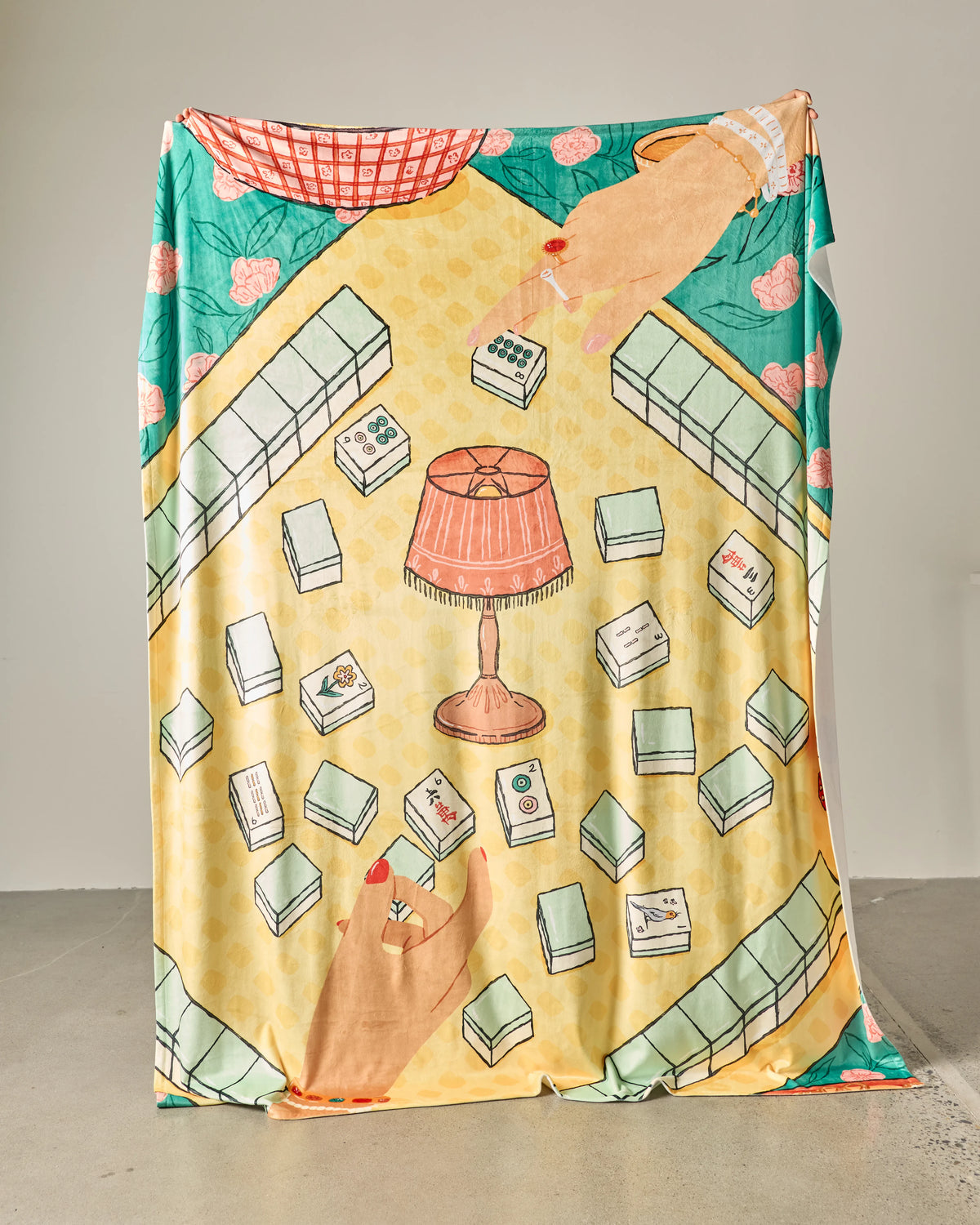 A hanging Geometry Lucky Hand Butter Blanket illustrated with a mahjong game in progress, featuring hands reaching for tiles around a central lamp.
