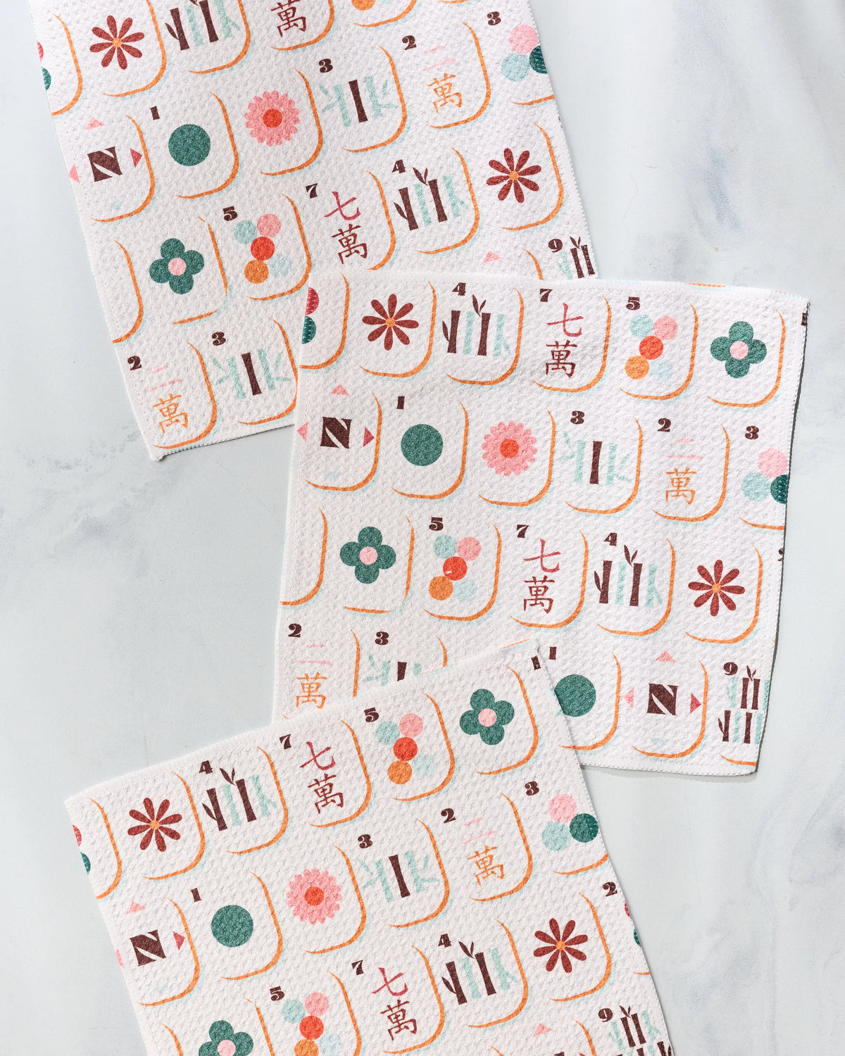 Three super-absorbent Geometry Cypress Tile Toss dishtowels with a repeating pattern of mahjong tiles featuring flowers, bamboo, characters, and numbers.
