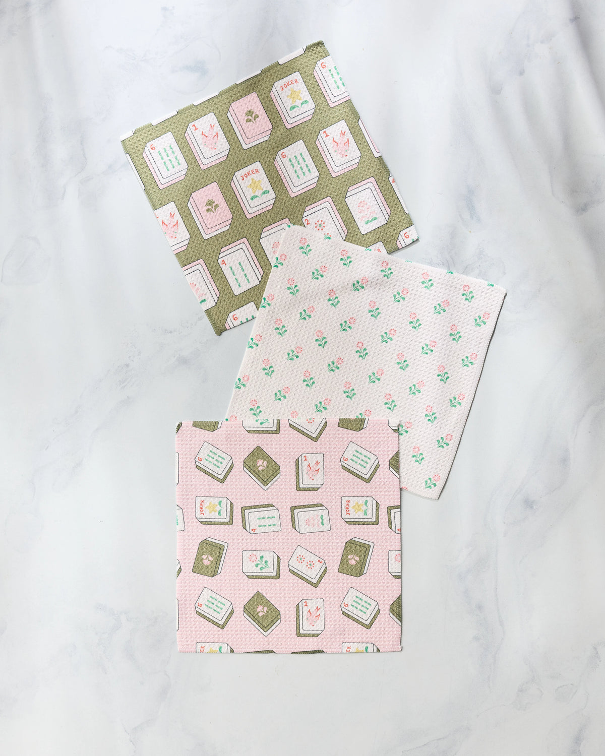 Three Flower Tiles super-absorbent dishtowels with patterns of mahjong tiles and pink flowers arranged on a marble surface.