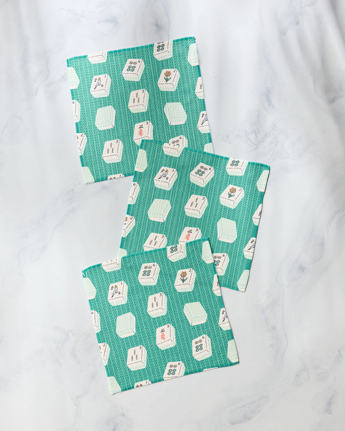 A set of three square, absorbent Geometry Tile Flow dishcloths featuring a teal background patterned with mahjong tile illustrations.