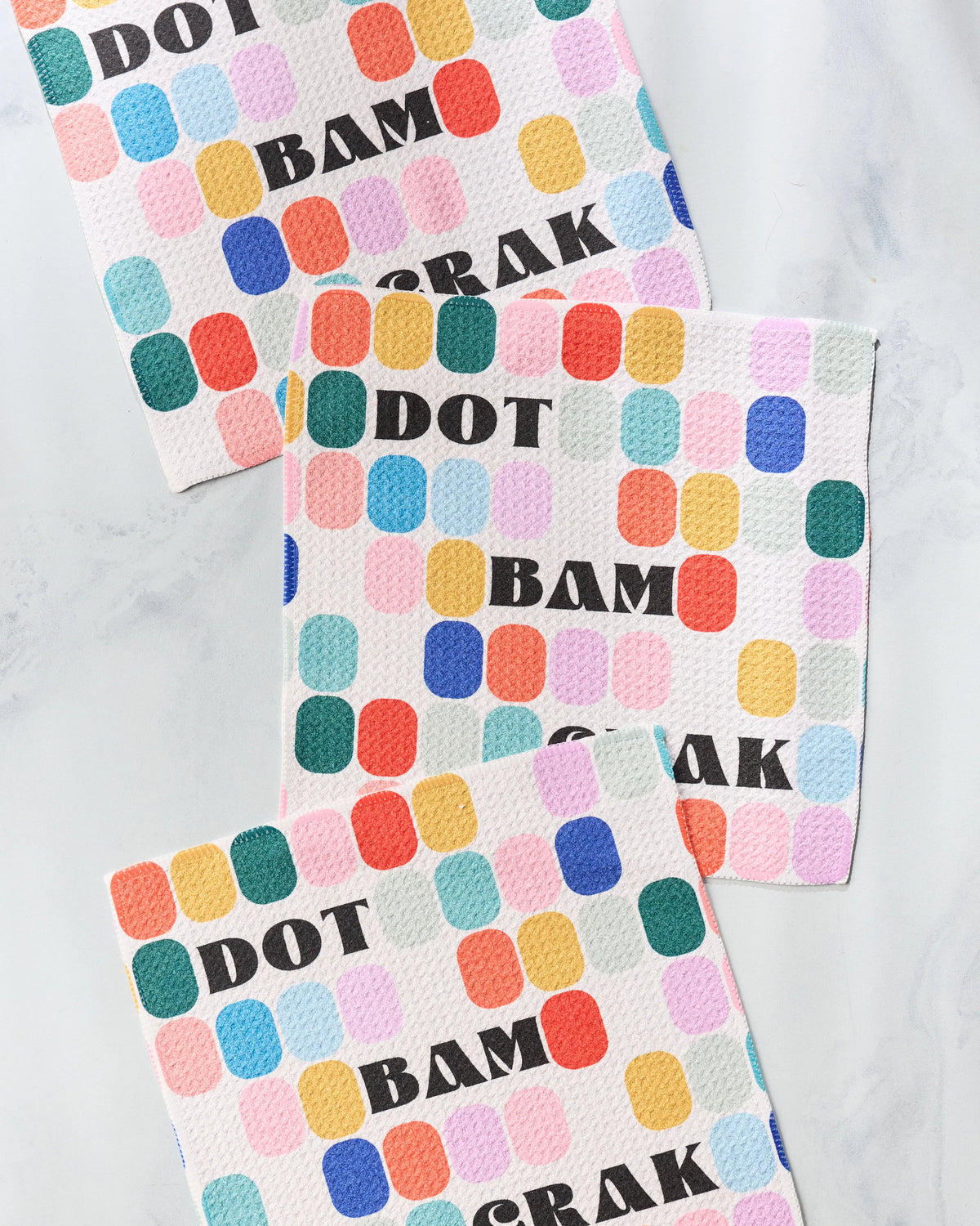 A set of three square Geometry Tile Talk kitchen cleaning cloths patterned with colorful rounded rectangles and the words DOT, BAM, and CRACK in black letters.