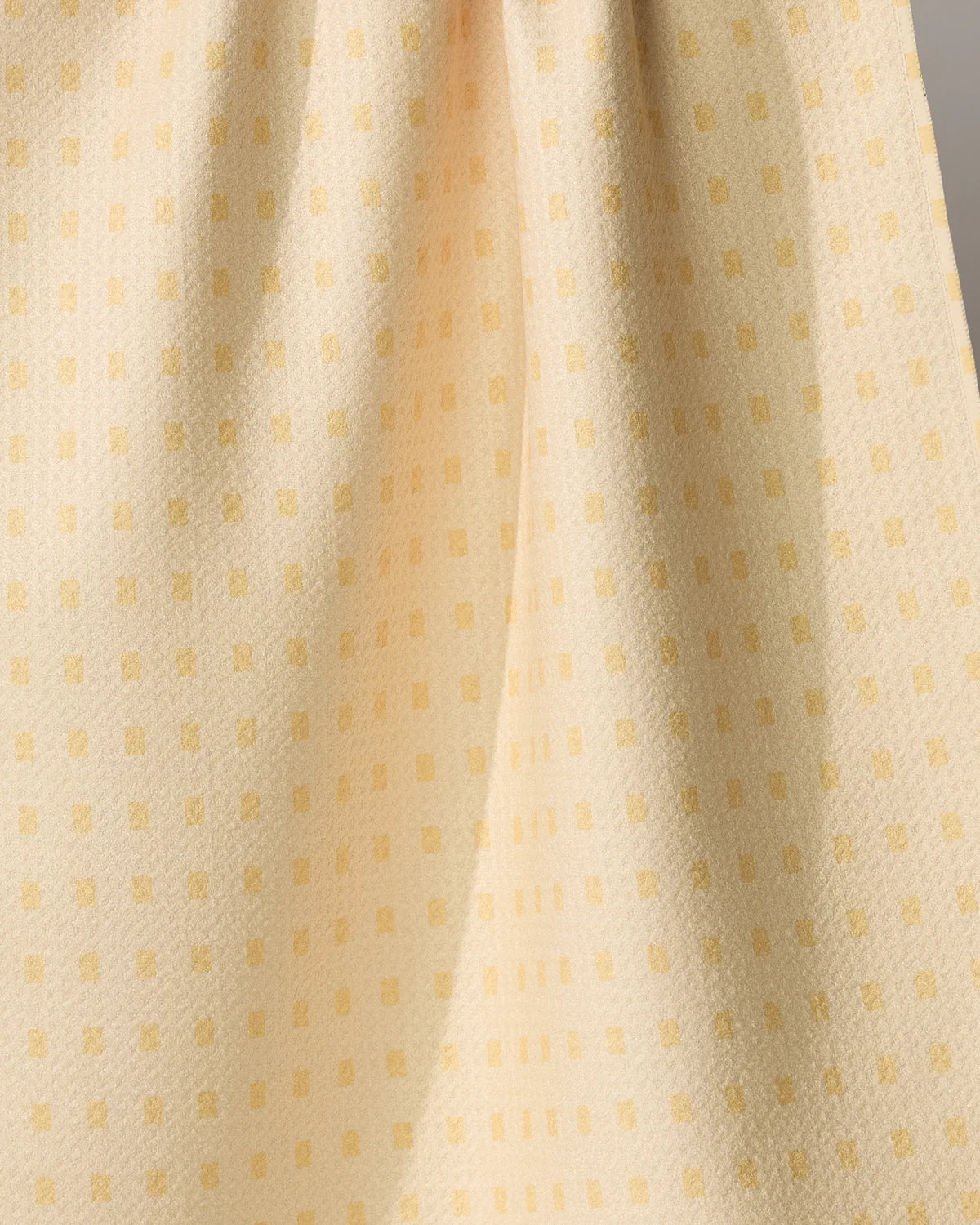A pale yellow Geometry Confetti Tiles tea towel featuring a repeating pattern of small, darker yellow rectangles.