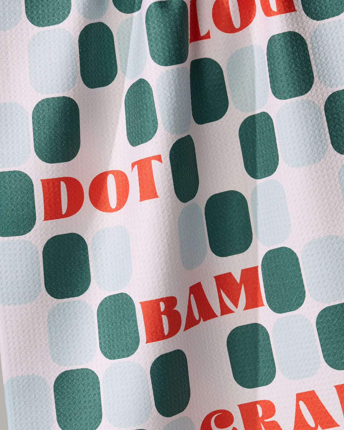 Geometry Cypress Tile Talk absorbent tea towel featuring a pattern of dark green and light blue rounded rectangles, interspersed with the red words DOT and BAM.