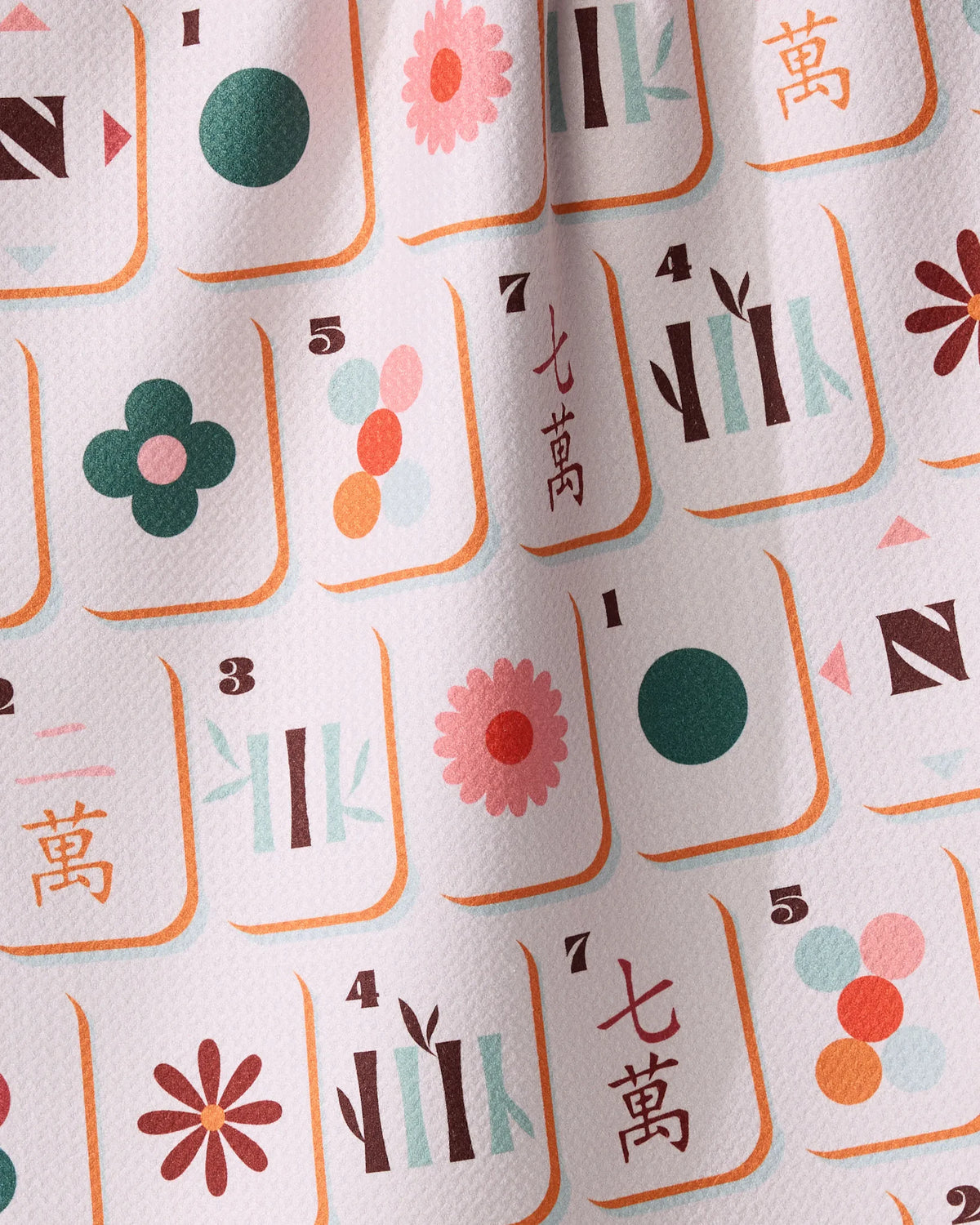 A repeating pattern of mahjong tiles featuring colorful flower icons, bamboo sticks, numbers, and Chinese characters on a light pink, quick-drying Geometry Cypress Tile Toss tea towel.