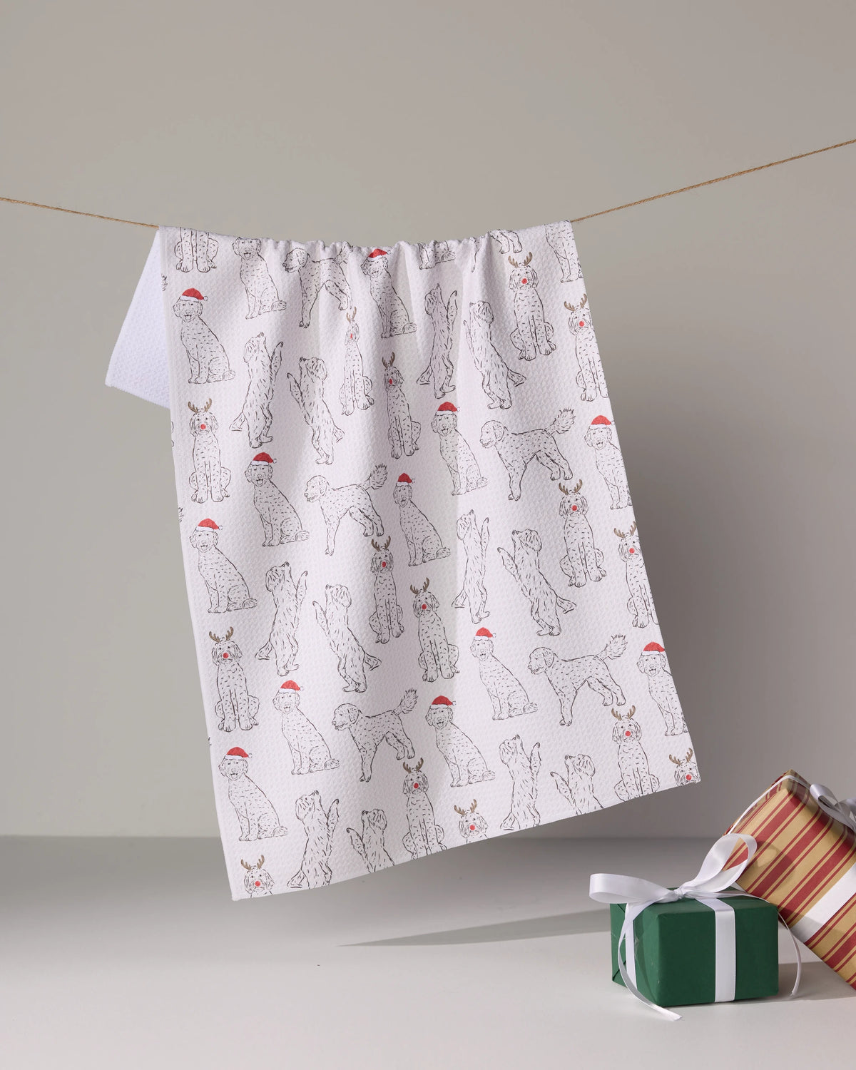 The Geometry Festive Doodles is a white, eco-friendly kitchen towel featuring black cat sketches in red Santa hats, hanging above two wrapped gift boxes—one striped, one green with a white ribbon.