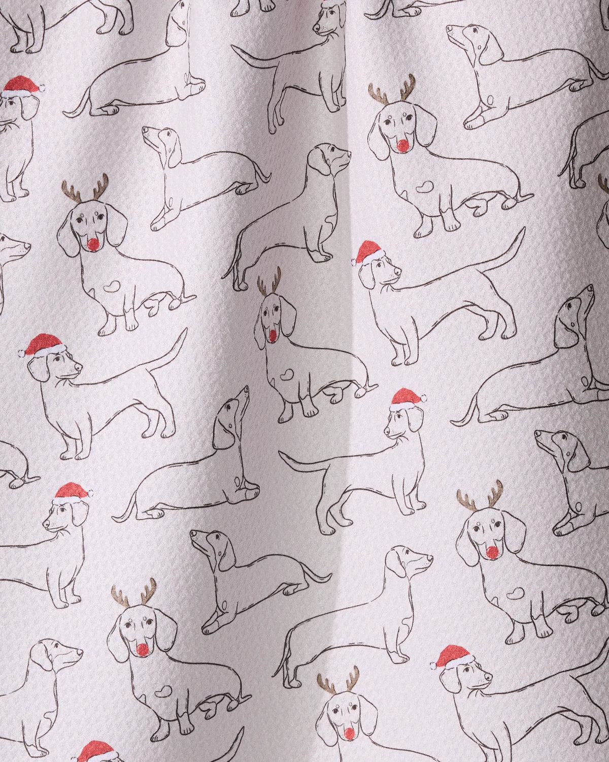 Festive Doxies by Geometry: a white textured tea towel made from recycled materials, featuring hand-drawn dachshunds with Santa hats and reindeer antlers.