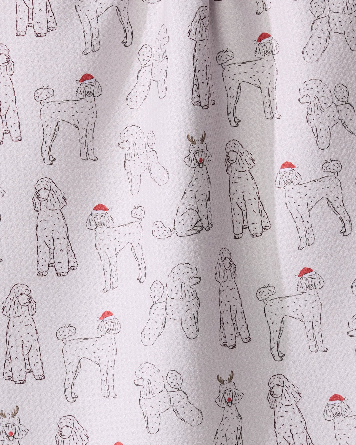The Festive Poodles tea towel by Geometry features poodle line drawings, most in Santa hats, one with reindeer antlers and a red nose. Light background, black outlines, and subtle red accents. Quick-drying design.