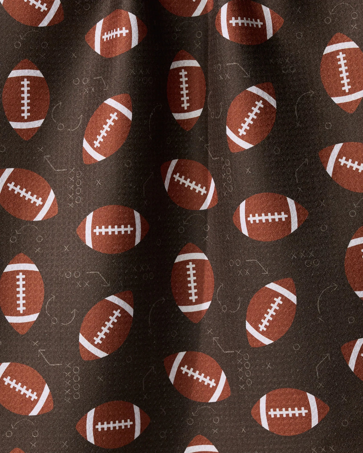 Brown Geometry First Down quick-drying tea towel patterned with footballs and faint white sketches of sports plays.