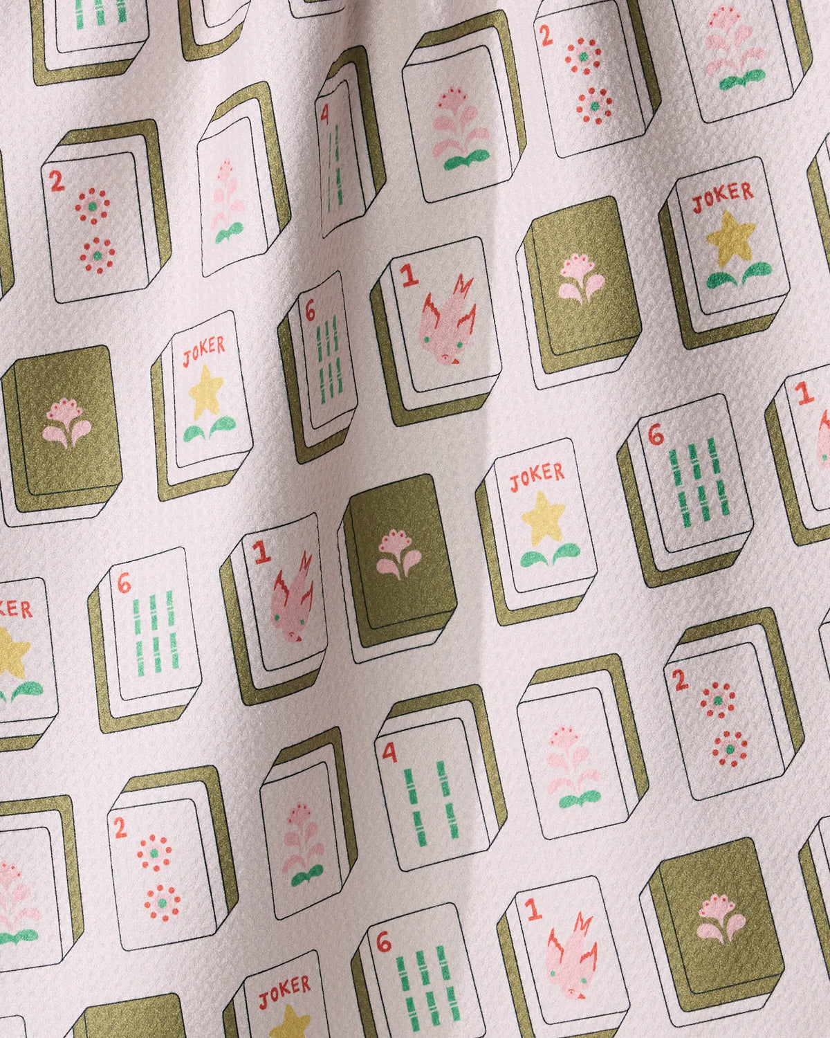 Flower Tiles tea towel in light pink, featuring a pattern of numbered mahjong tiles and Joker tiles decorated with flowers and stars.