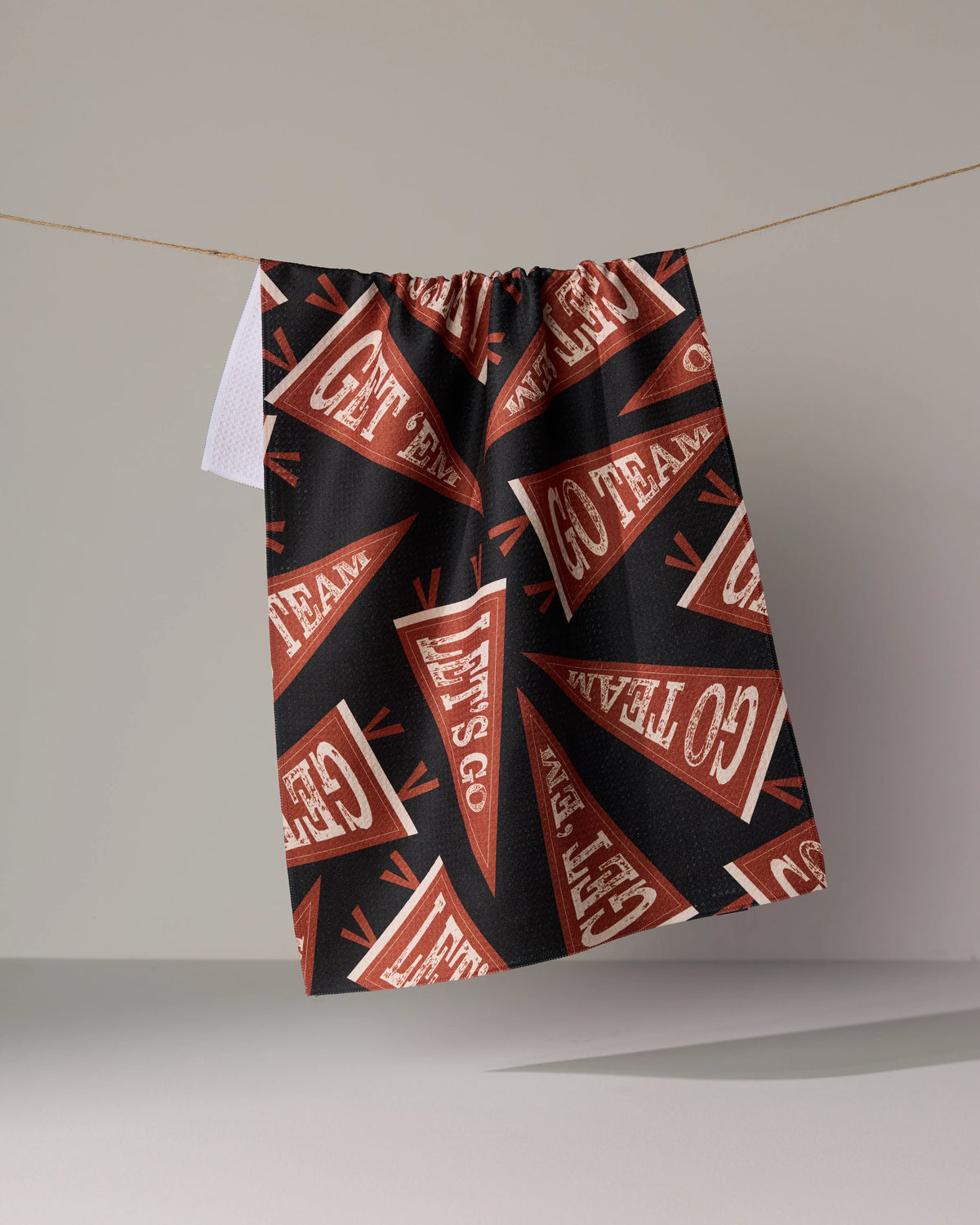 Geometry Football Chant black tea towel featuring a repeating pattern of dark red pennants printed with the phrases GET EM and GO TEAM hanging from a string.