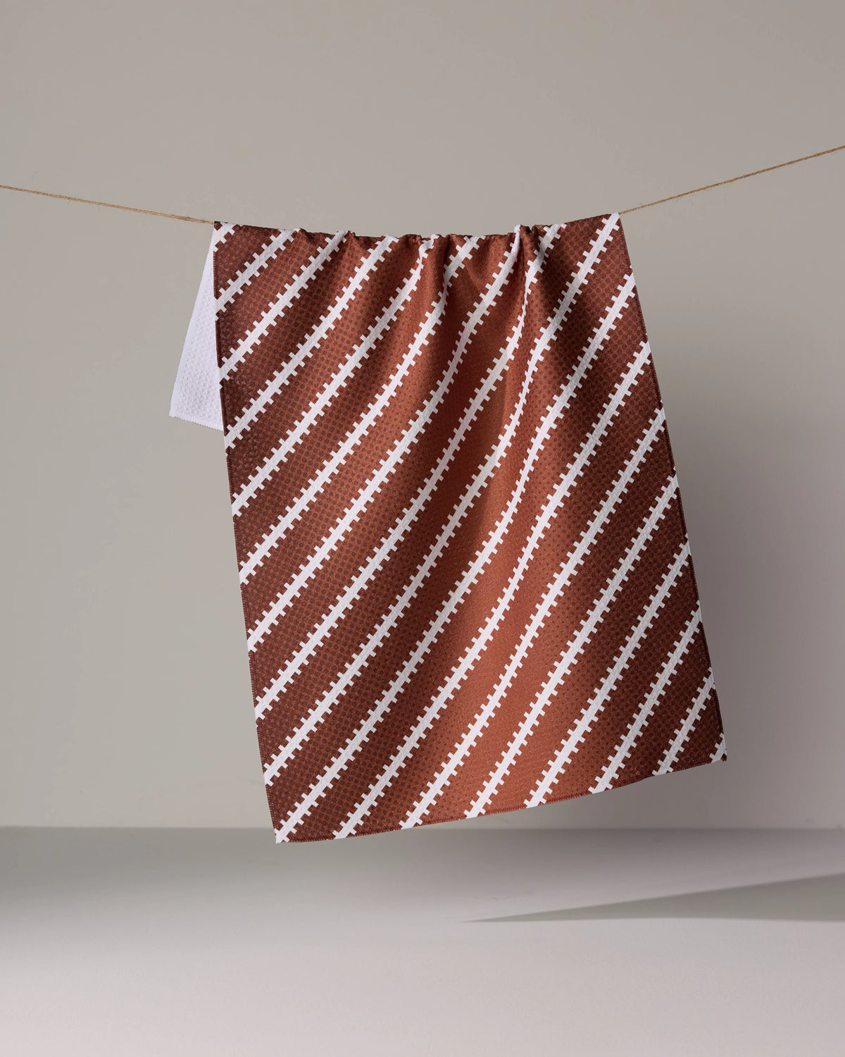 A Laces Out kitchen towel in ultra-absorbent brown with a white football-themed pattern hanging on a clothesline.