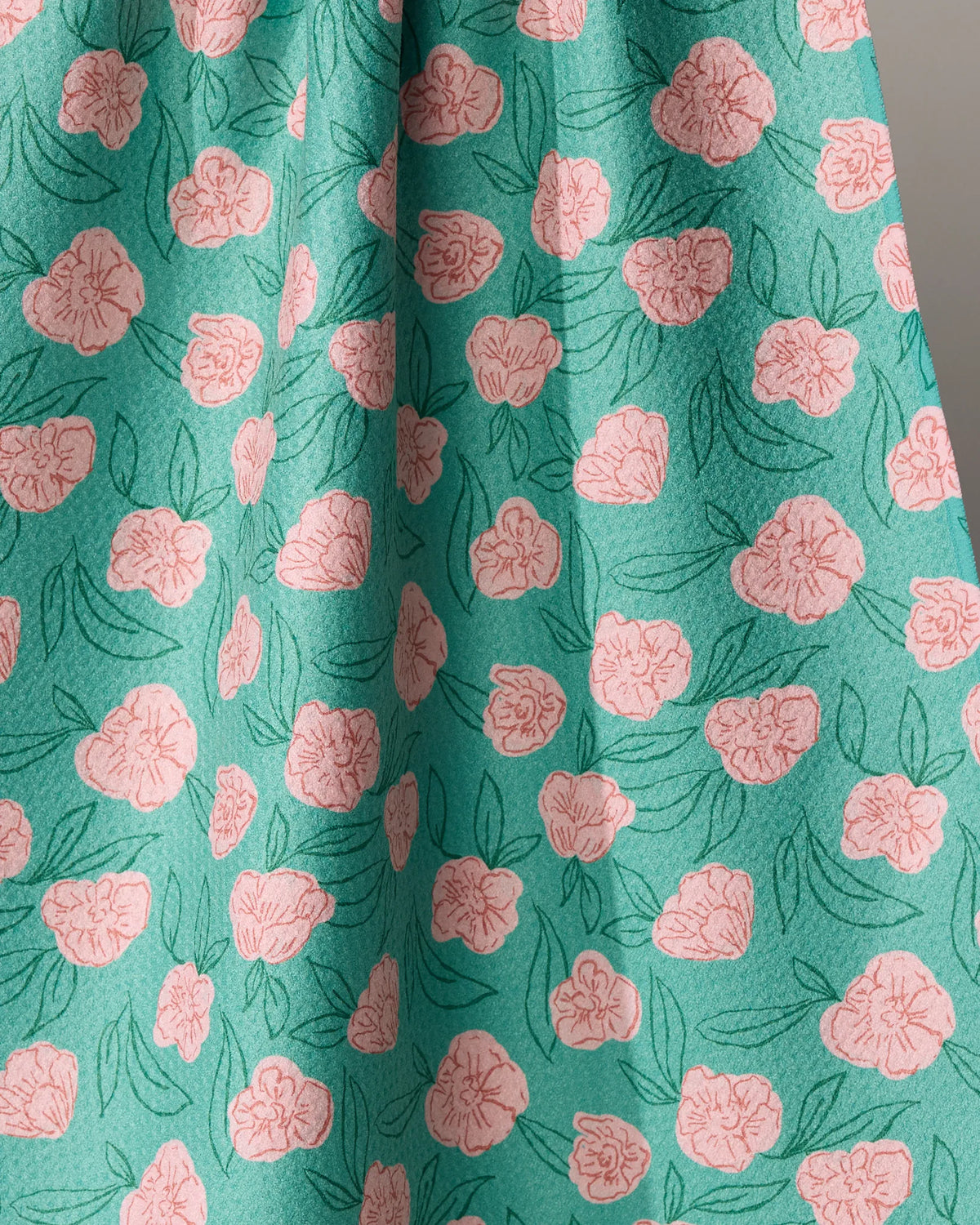 This Lucky Bloom recycled kitchen towel features a repeating pattern of pink line-drawn flowers and dark green leaves on a teal background.