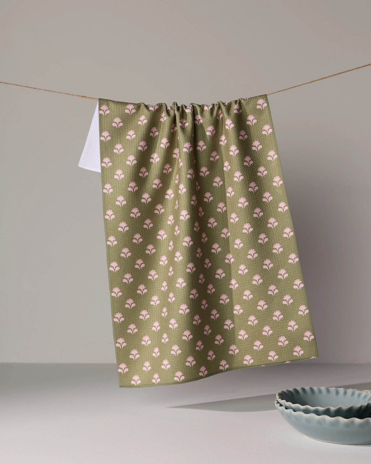 Lucky Flowers kitchen towel in an ultra-absorbent olive green featuring a repeating pattern of small pink flowers hanging on a clothesline.