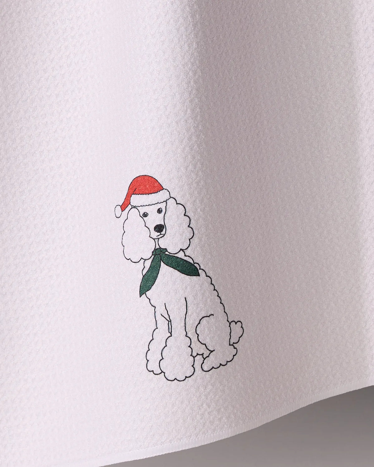 The Geometry Merry Poodle kitchen towel features a white poodle in a red Santa hat and green scarf, printed on absorbent, textured white fabric.