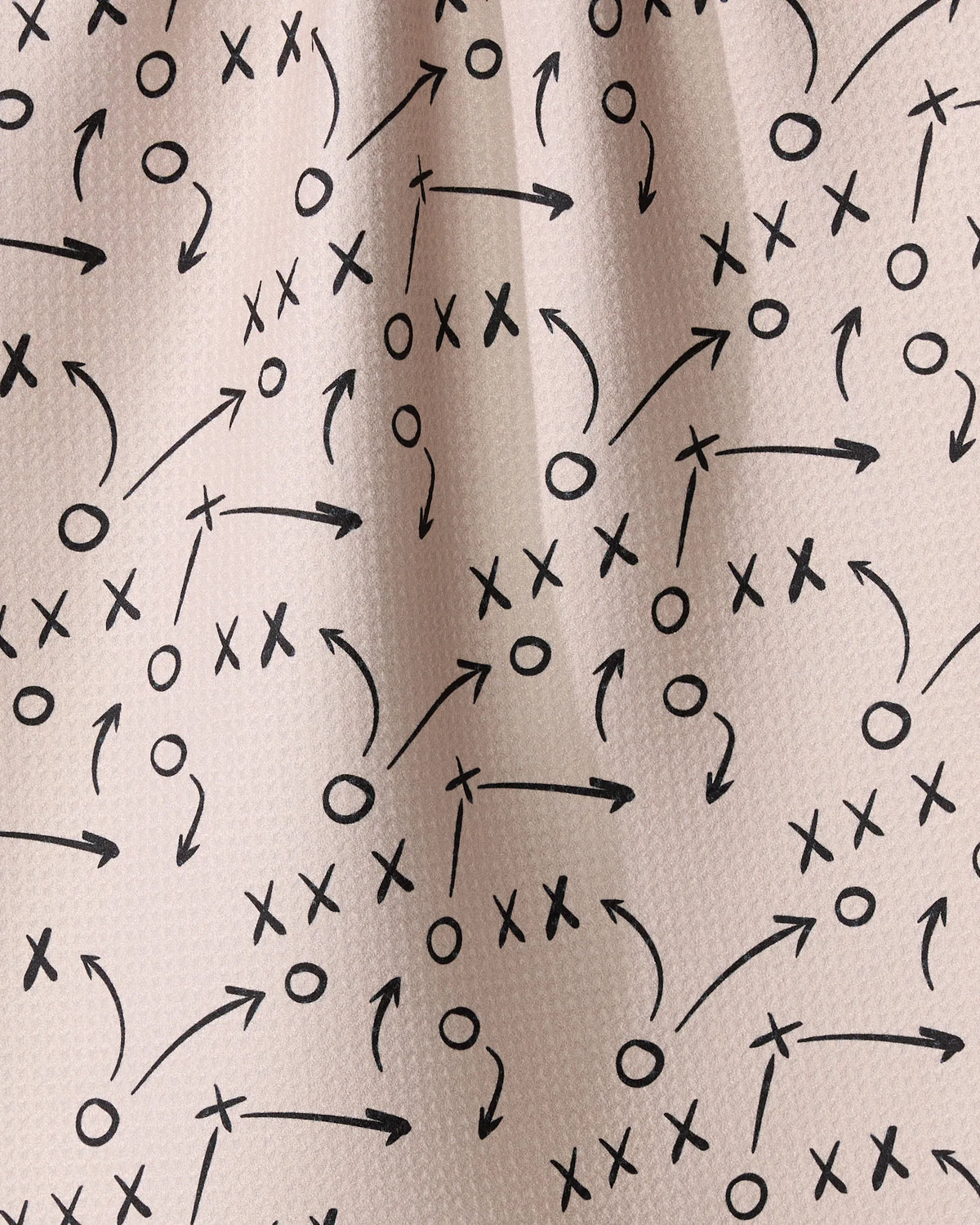 Light-colored Geometry Playbook kitchen towel patterned with black hand-drawn diagrams of Xs, Os, and directional arrows similar to sports plays.