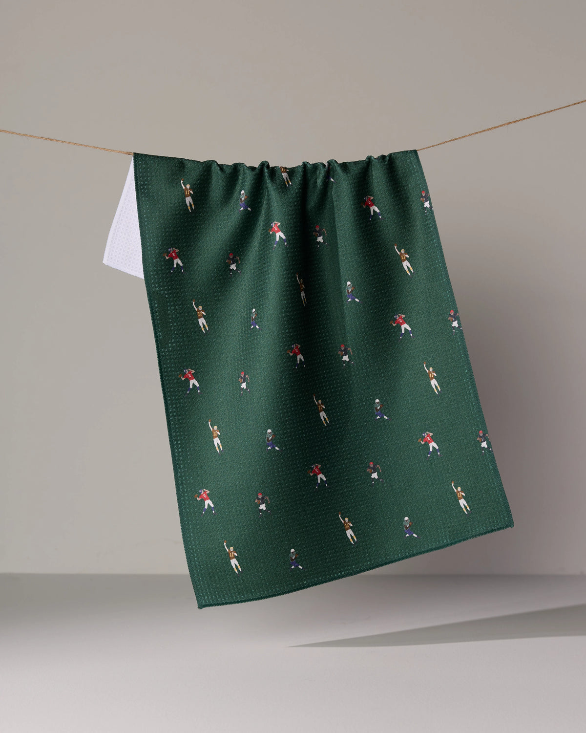 Dark green quick-drying Geometry Roster tea towel hanging from a string, patterned with small illustrations of football players in various uniforms.