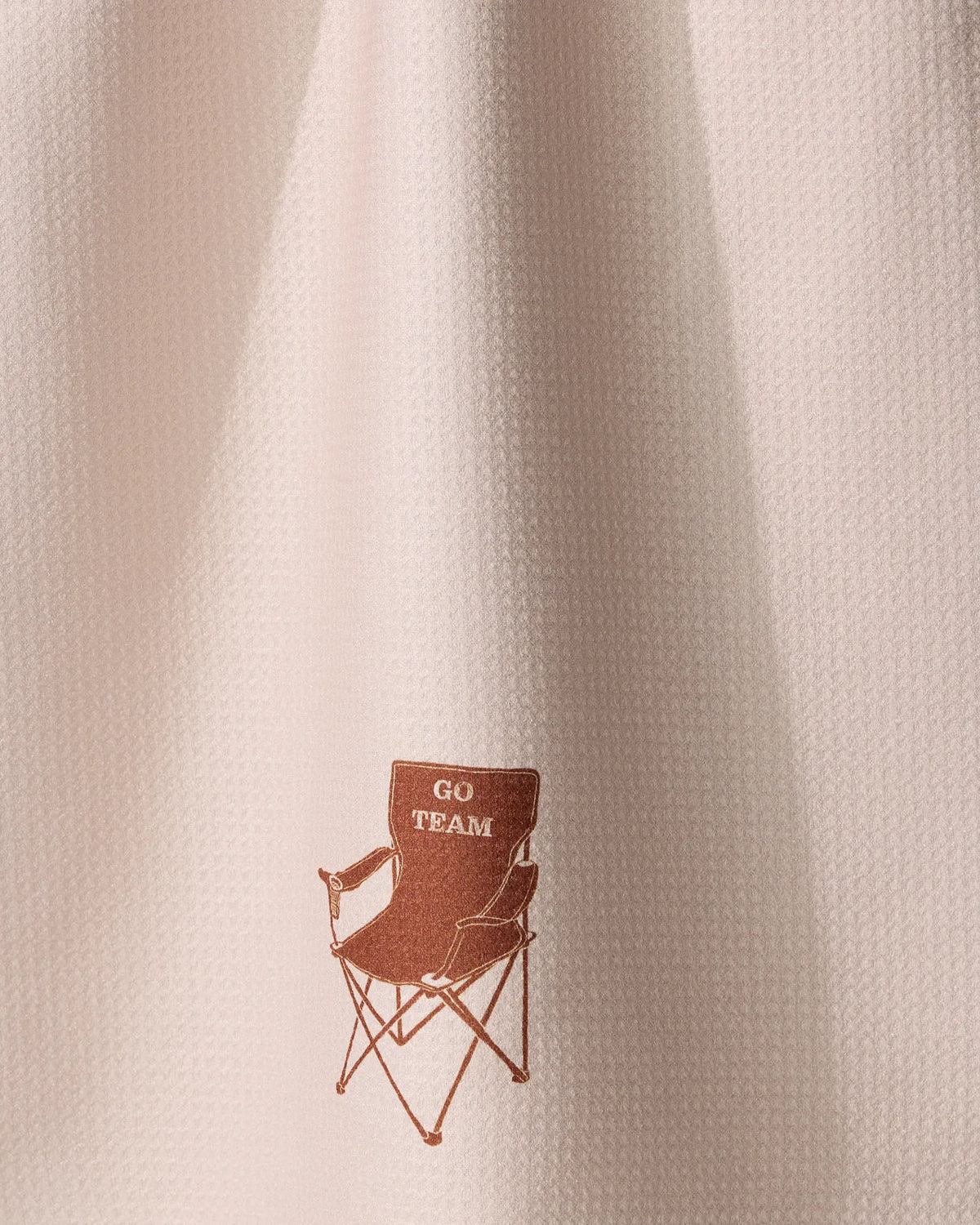 Geometry Tailgate light pink textured recycled kitchen towel featuring a small brown illustration of a folding chair with the text GO TEAM on the backrest.