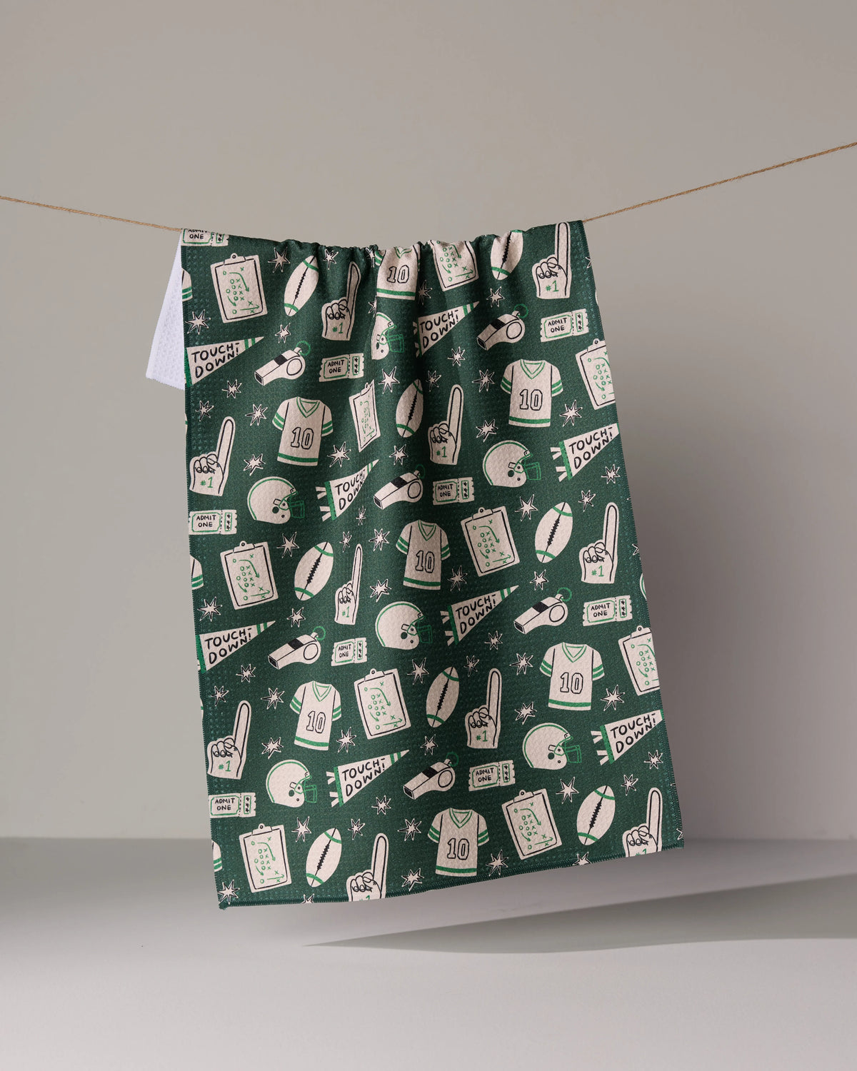 Dark green Team Huddle recycled kitchen towel featuring an all-over pattern of football-themed illustrations including jerseys, helmets, whistles, playbooks, and foam fingers.