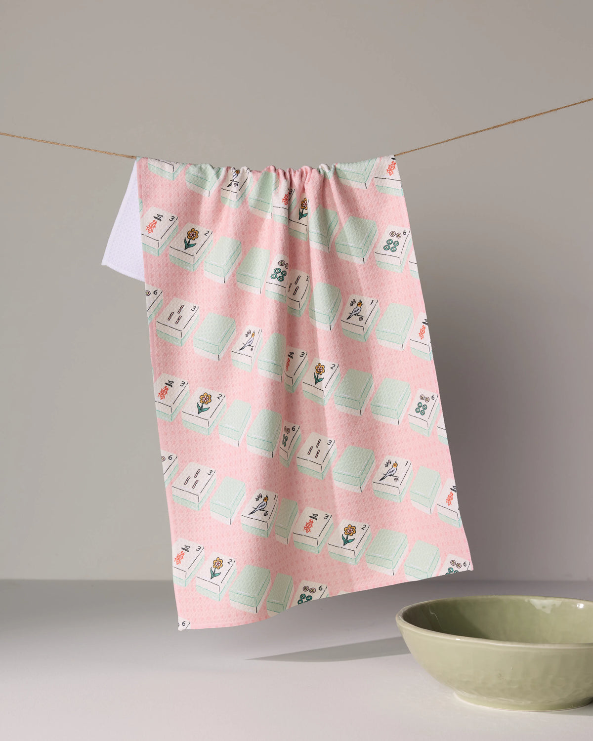 A quick-drying pink Tile Parade tea towel patterned with mahjong tiles hanging on a line.