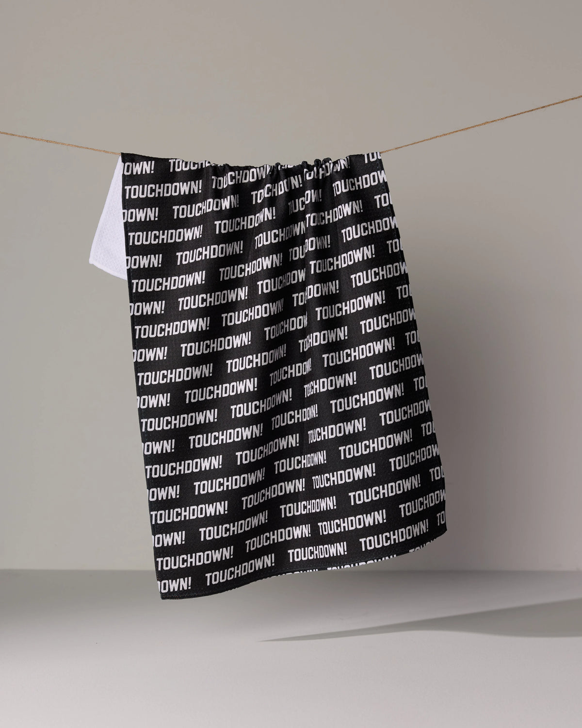 A black absorbent Geometry Touchdown dish towel hangs on a clothesline, featuring the word TOUCHDOWN! repeated in white text.