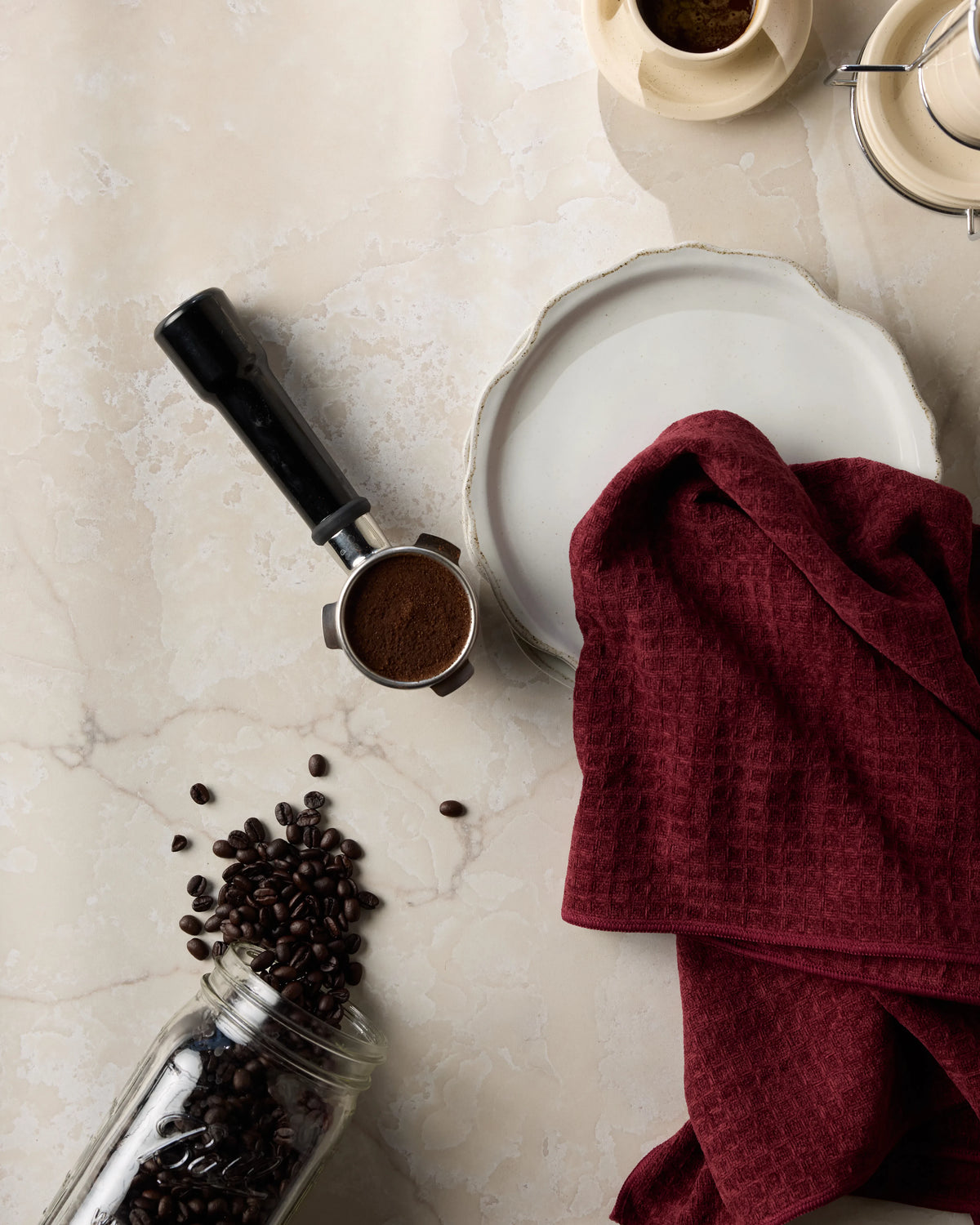 The Merlot by Geometry is displayed on a marble countertop alongside a portafilter with ground coffee and a spilled jar of coffee beans.