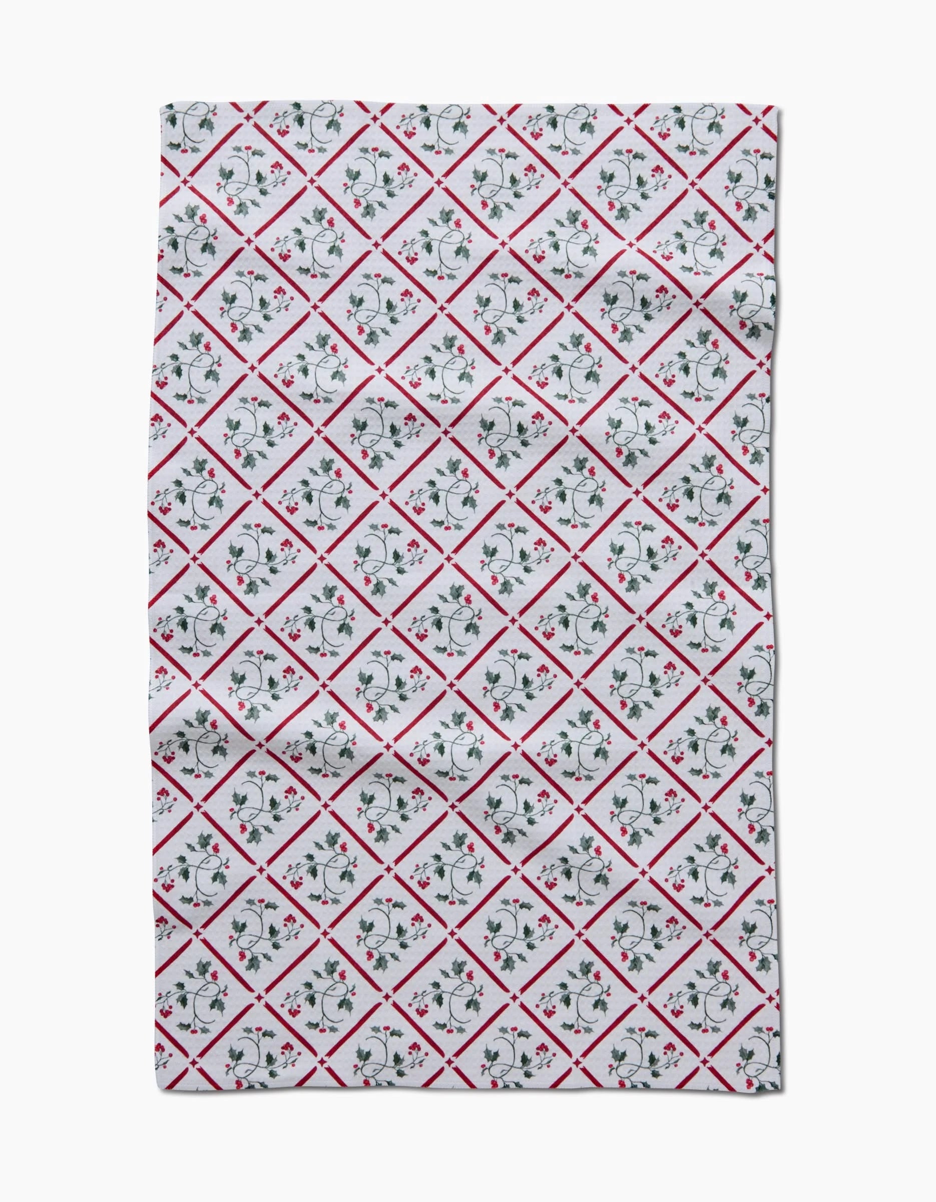 The Aubrey Fairchild Christmas Mistletoe Trellis Luxe Hand Towel features Geoweave technology, a white cloth with a red-bordered diamond grid, and green and red floral motifs. The quick-drying fabric is shown flat with slight wrinkles.