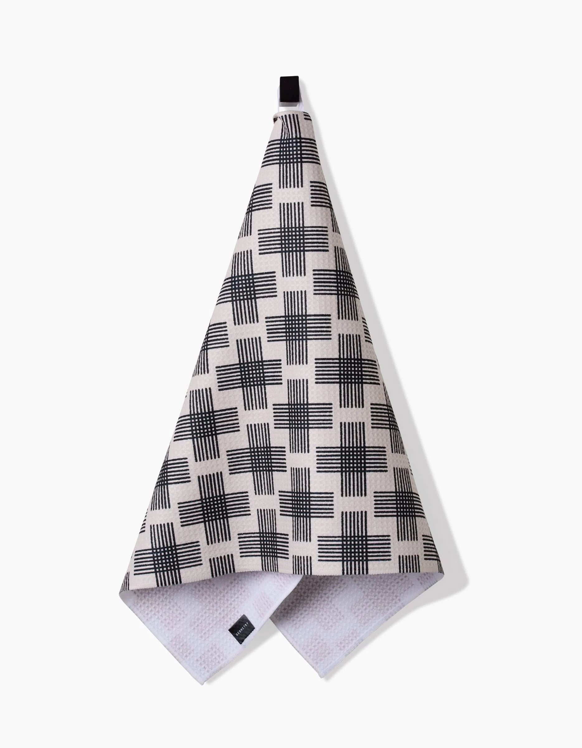 The Rosa Kichline Cross Hatch is a beige hanging kitchen towel with a black geometric crosshatch pattern, made with ultra-absorbent Geoweave technology and a black hanging loop, shown against a white background.
