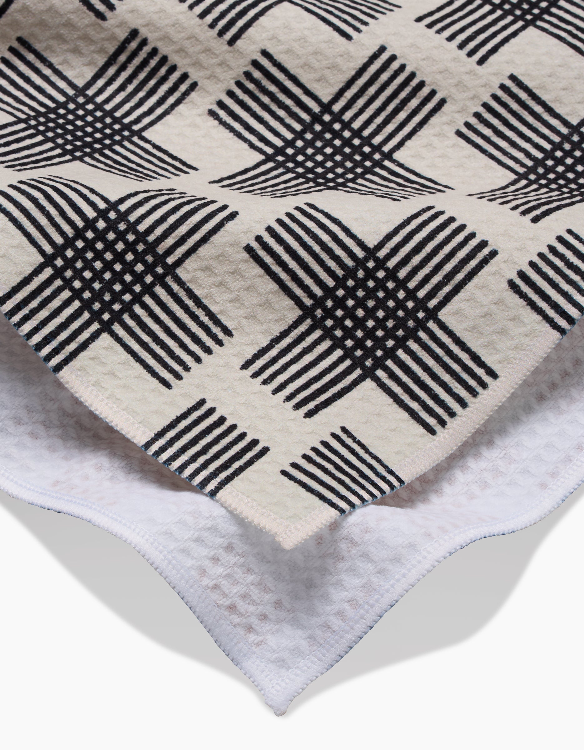 A close-up of Cross Hatch by Rosa Kichline: the beige top layer features a black geometric checkered pattern over a white, waffle-textured base, crafted with Geoweave technology for an ultra-absorbent Luxe Hand Towel finish.
