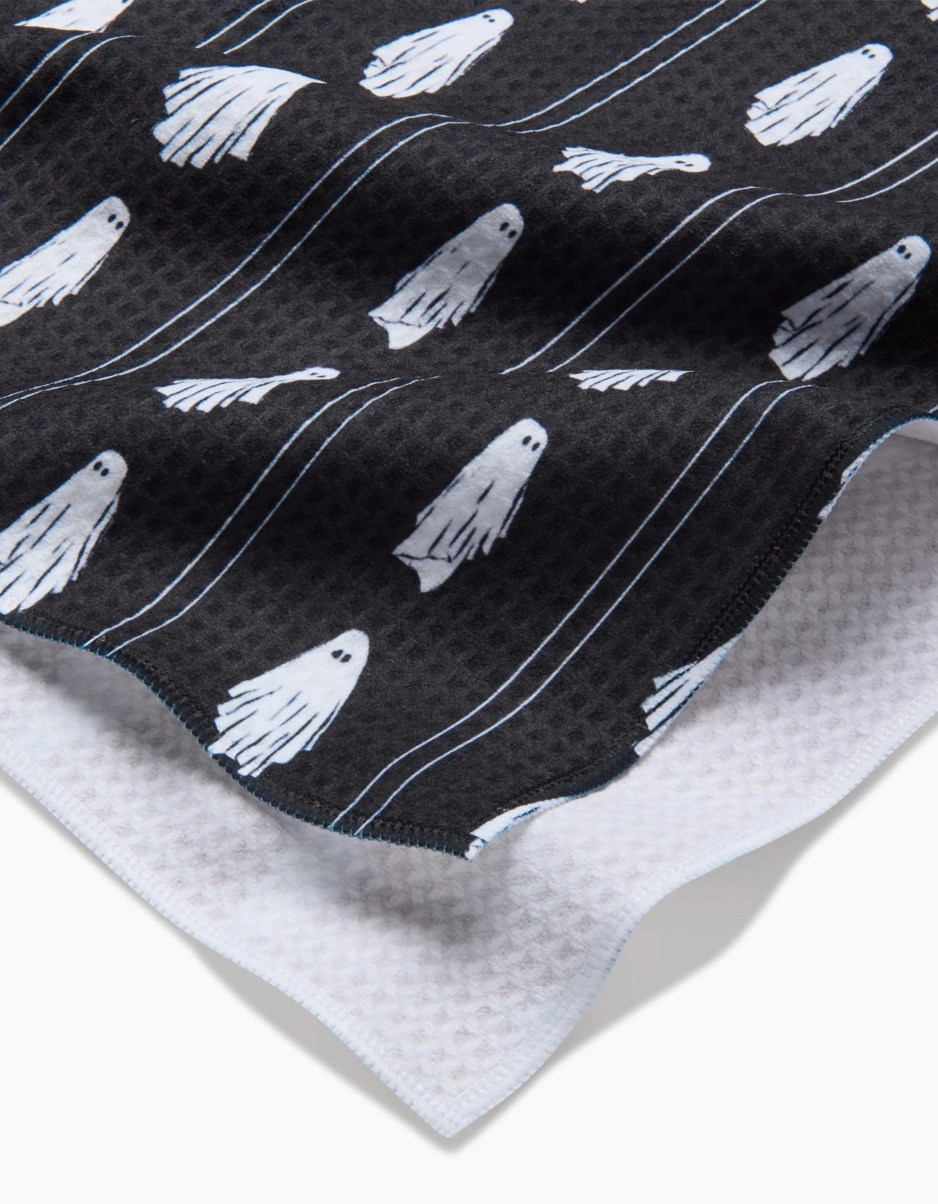 The Aubrey Fairchild Ghost Pinstripes Luxe Hand Towel in black features small white cartoon ghosts and thin white lines, crafted from recycled materials, and rests atop a white textured fabric.