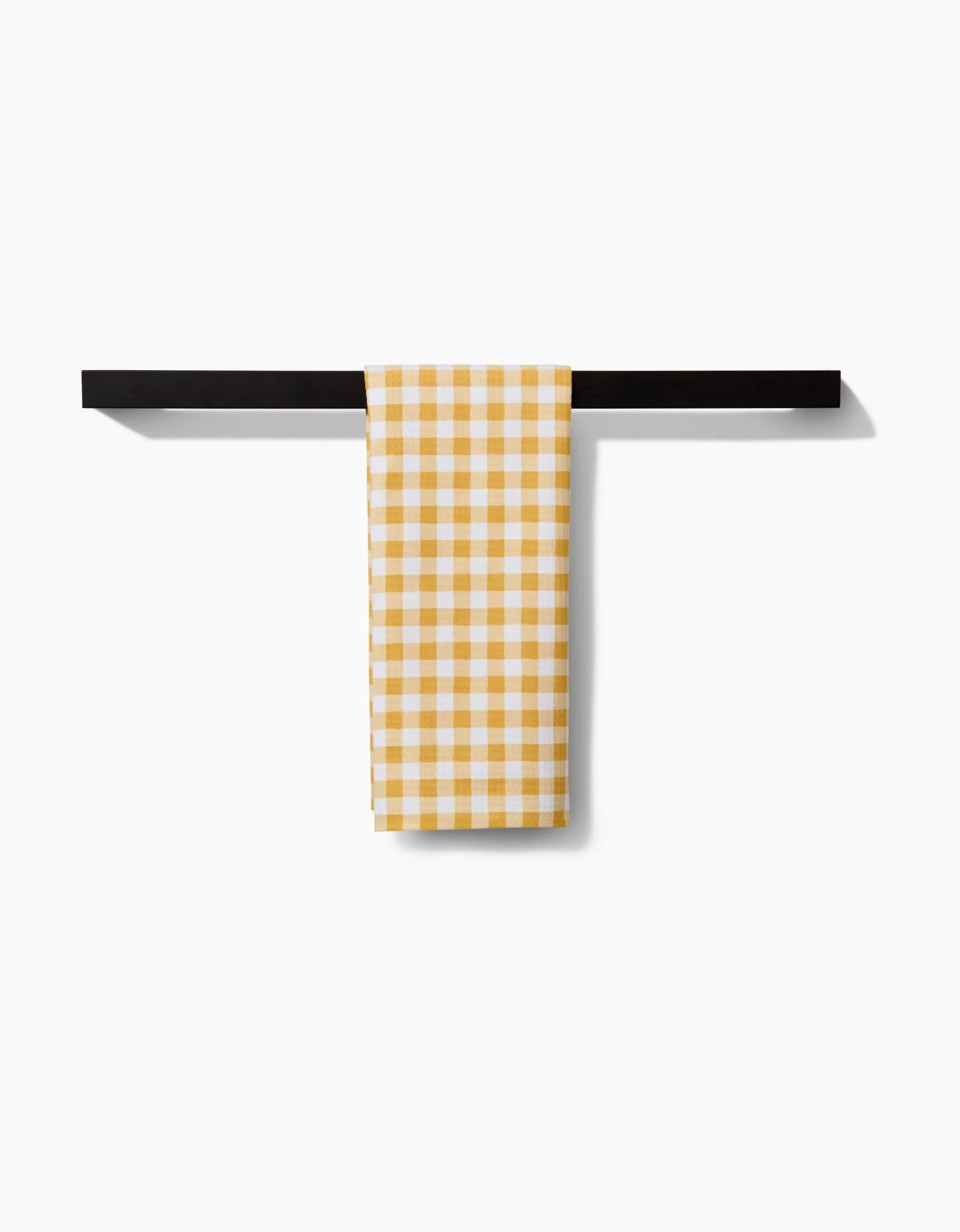 The Danelys Sidron Golden Plaid hand towel, featuring a yellow and white check pattern, ultra-absorbent and neatly folded, hangs on a simple black bar against a plain white background.