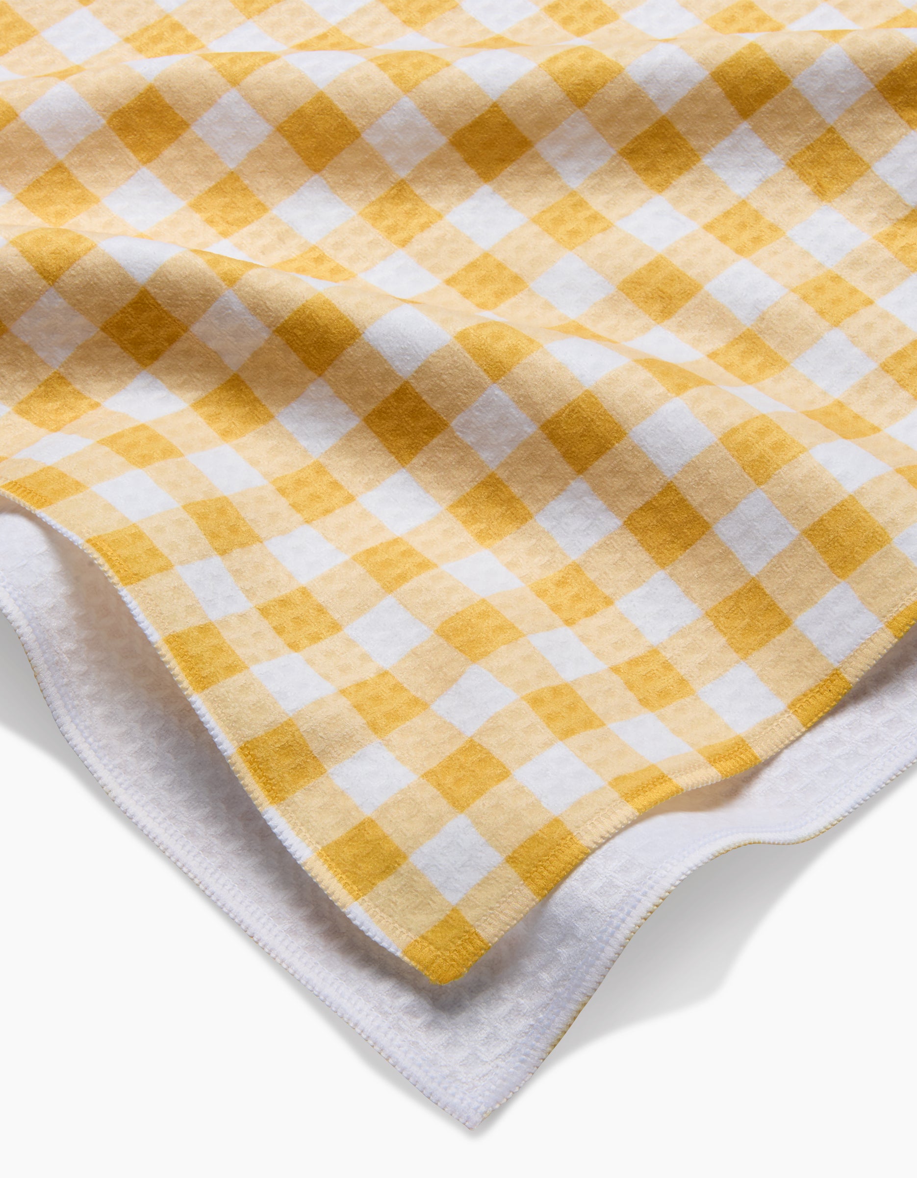 The Golden Plaid by Danelys Sidron is a soft, ultra-absorbent fabric featuring a yellow and white checkered gingham pattern, shown slightly folded to reveal its white underside.