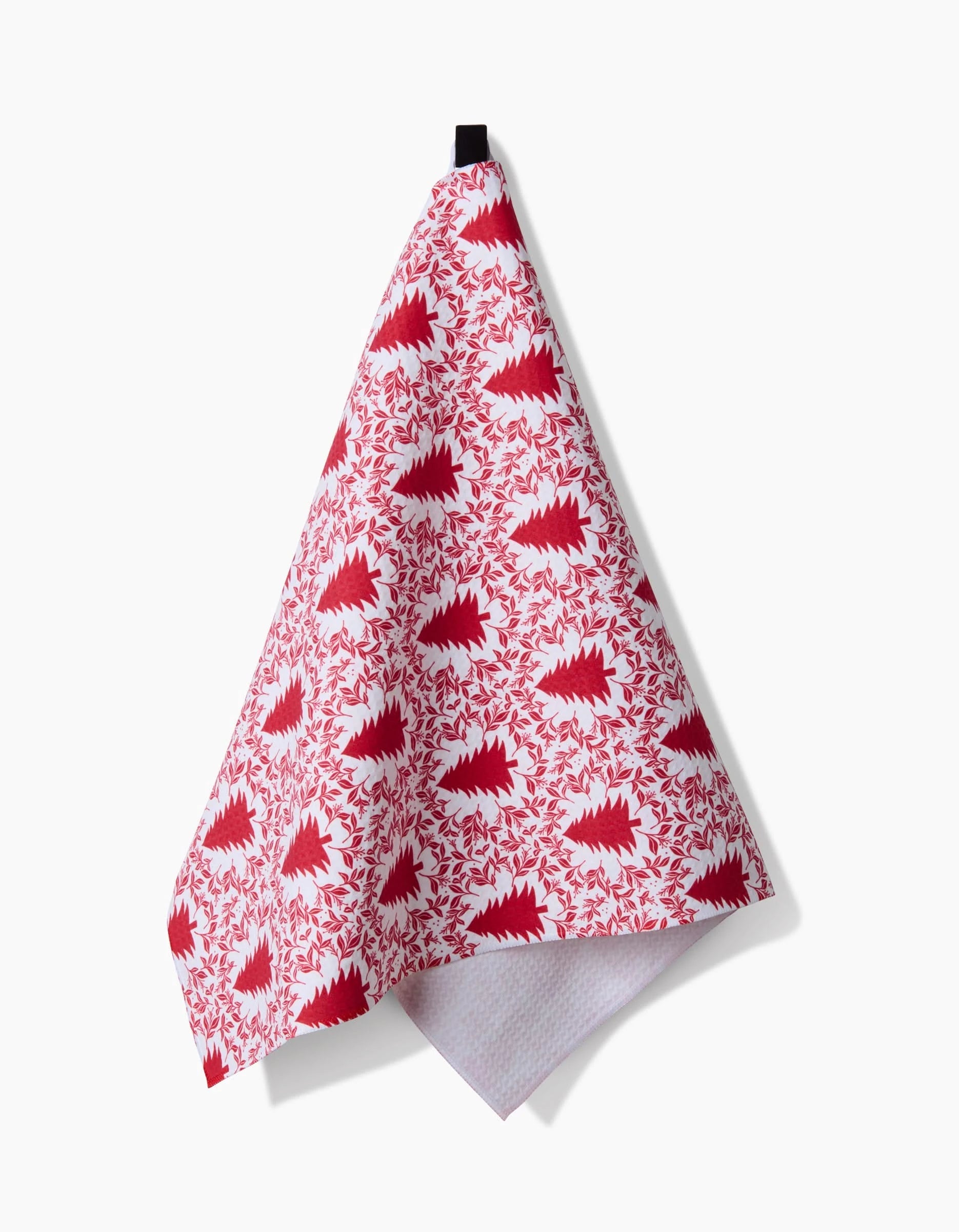 A Holiday Tree hand towel by Charlie Rowan Designs, featuring a white base with red and pink stylized hedgehogs and leaves in a repeating pattern and quick-drying Geoweave technology, hangs from a black loop on a white background.