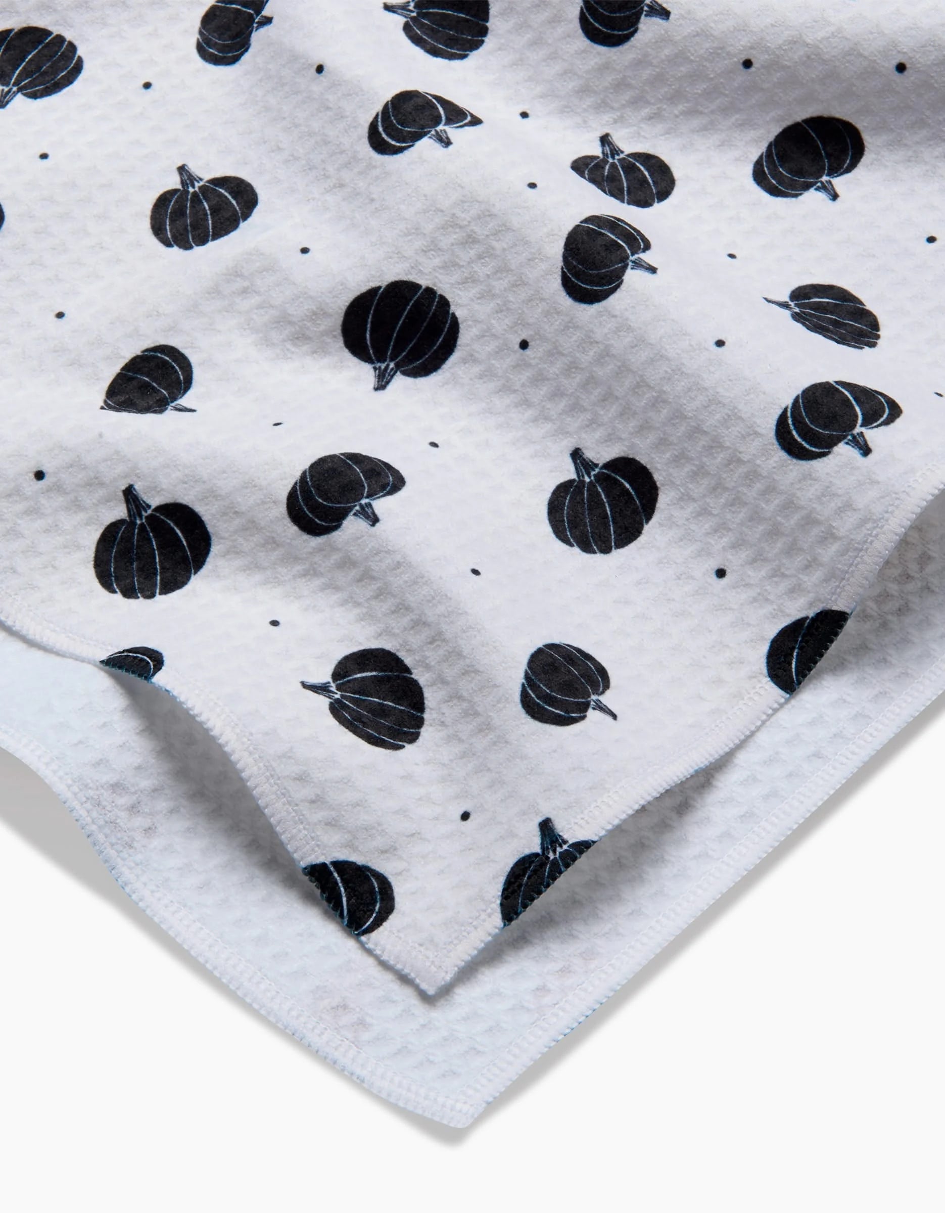 A close-up of Ash Cascade’s Midnight Pumpkin Luxe Hand Towel, showcasing white textured Geoweave fabric with a repeating black pumpkin and dot pattern and visible layered edges for an ultra-absorbent finish.