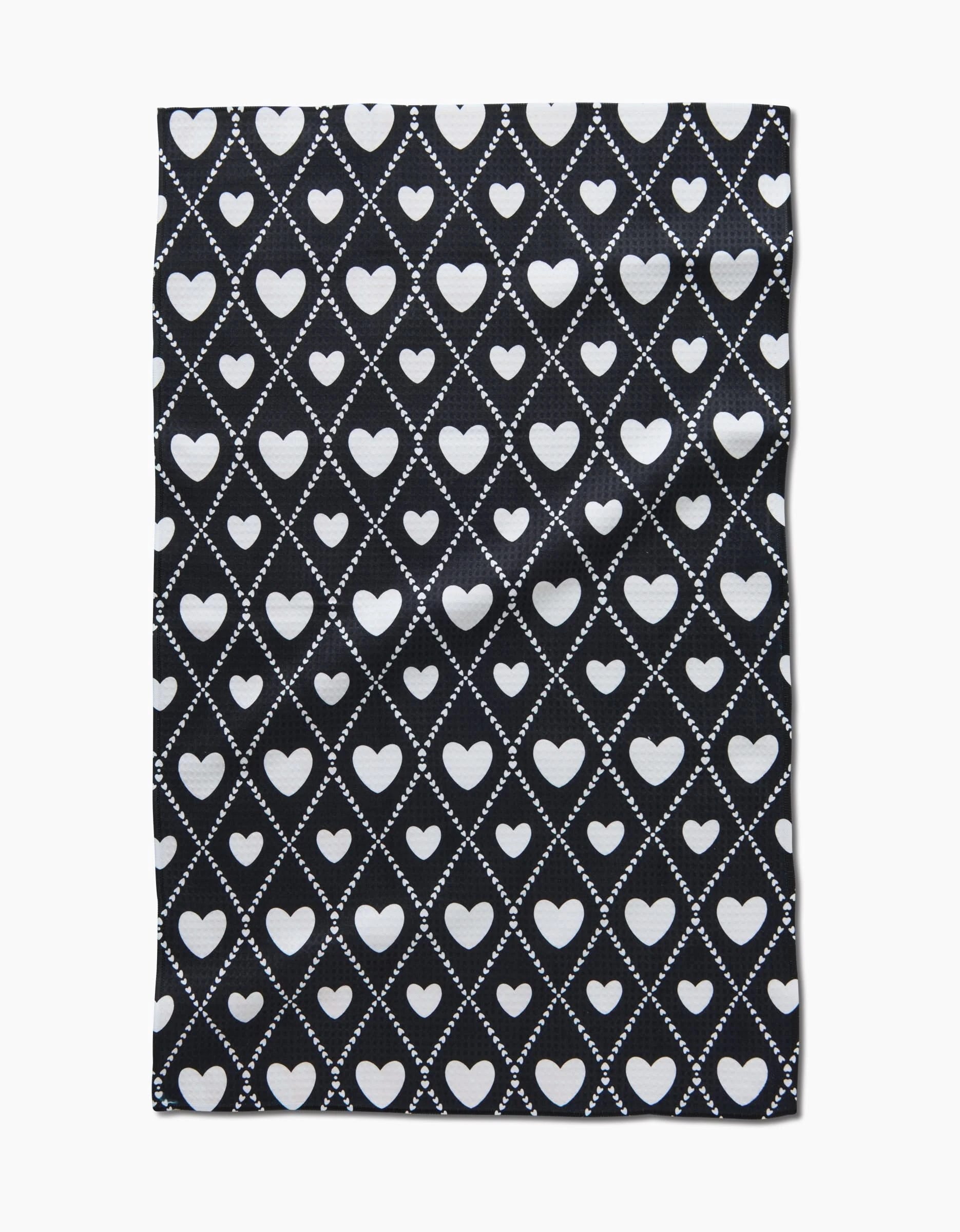 The Onyx Love Lattice hand towel by Charlie Rowan Designs is black, sustainably made from recycled materials, and features white hearts within diamond patterns formed by dotted lines.