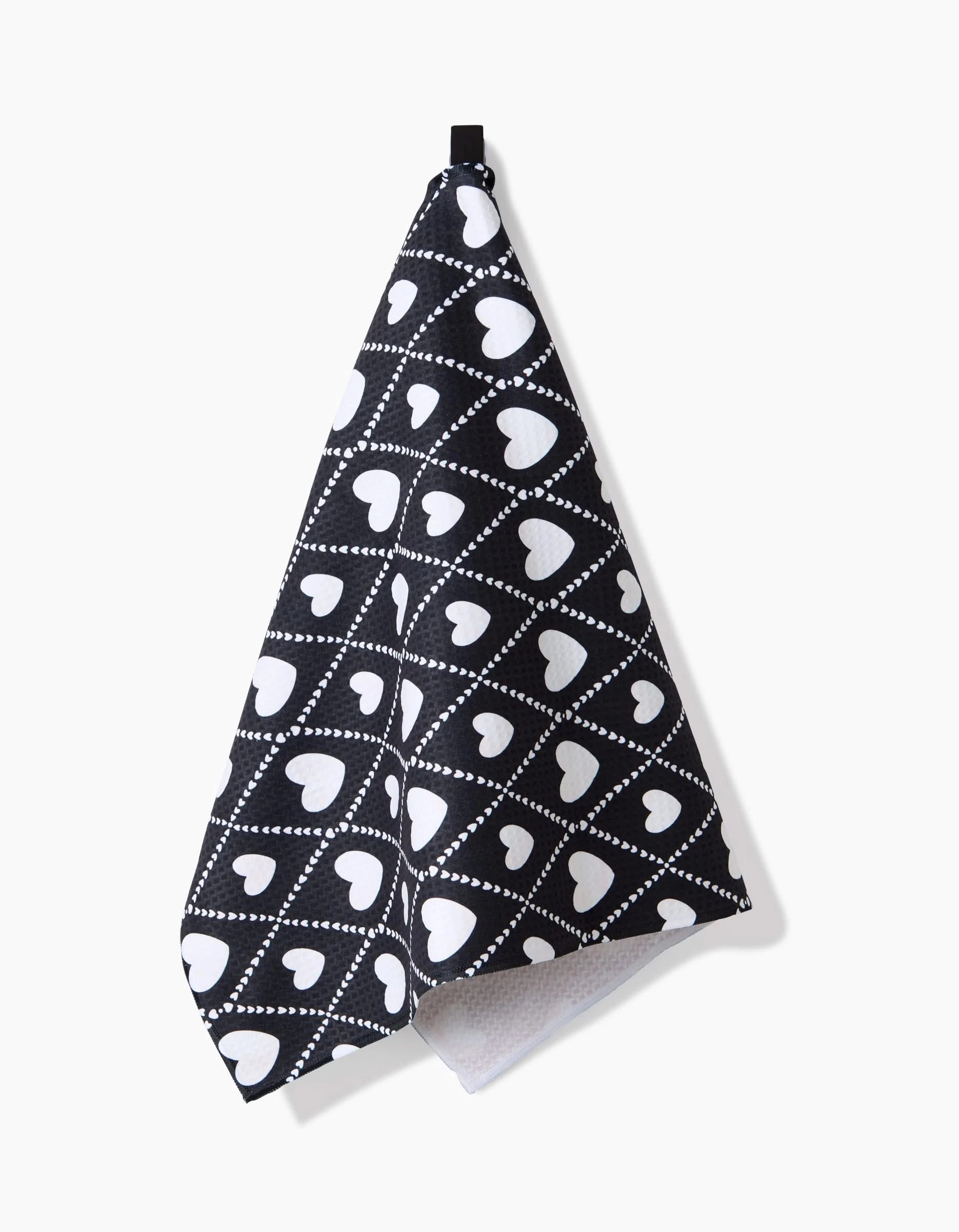The Onyx Love Lattice hand towel by Charlie Rowan Designs is black, made from recycled materials, and showcases white hearts with dotted diagonal lines on a white background.