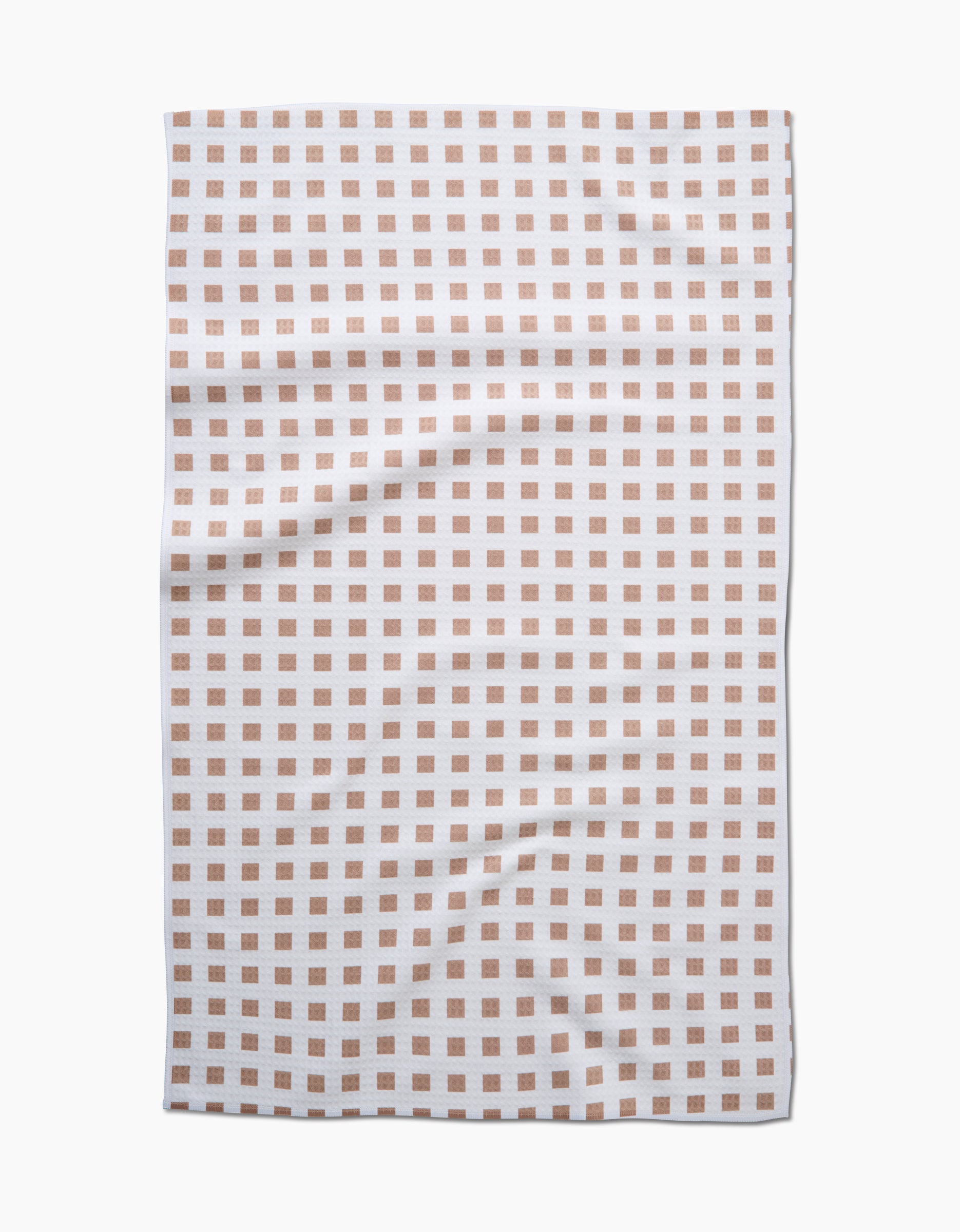 The GEOMETRY Spring Square towel features evenly spaced light brown squares on white, photographed from above with a slightly wrinkled look. Made with quick-drying Geoweave technology for both convenience and style.