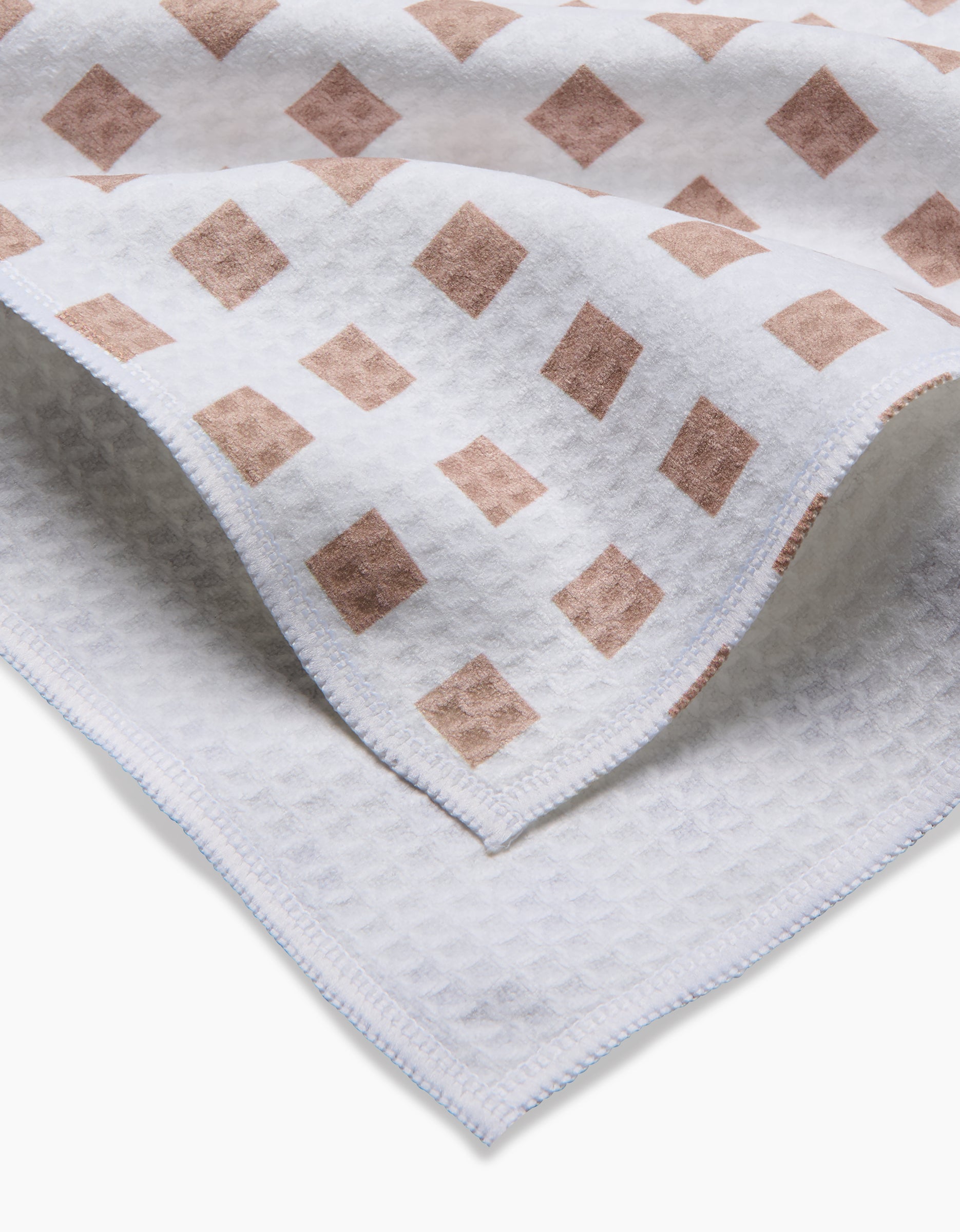 A close-up of the GEOMETRY Spring Square towel, featuring a white ultra-absorbent waffle texture, neatly stitched edges, and a corner adorned with light brown diamond shapes. This towel is designed for quick drying.